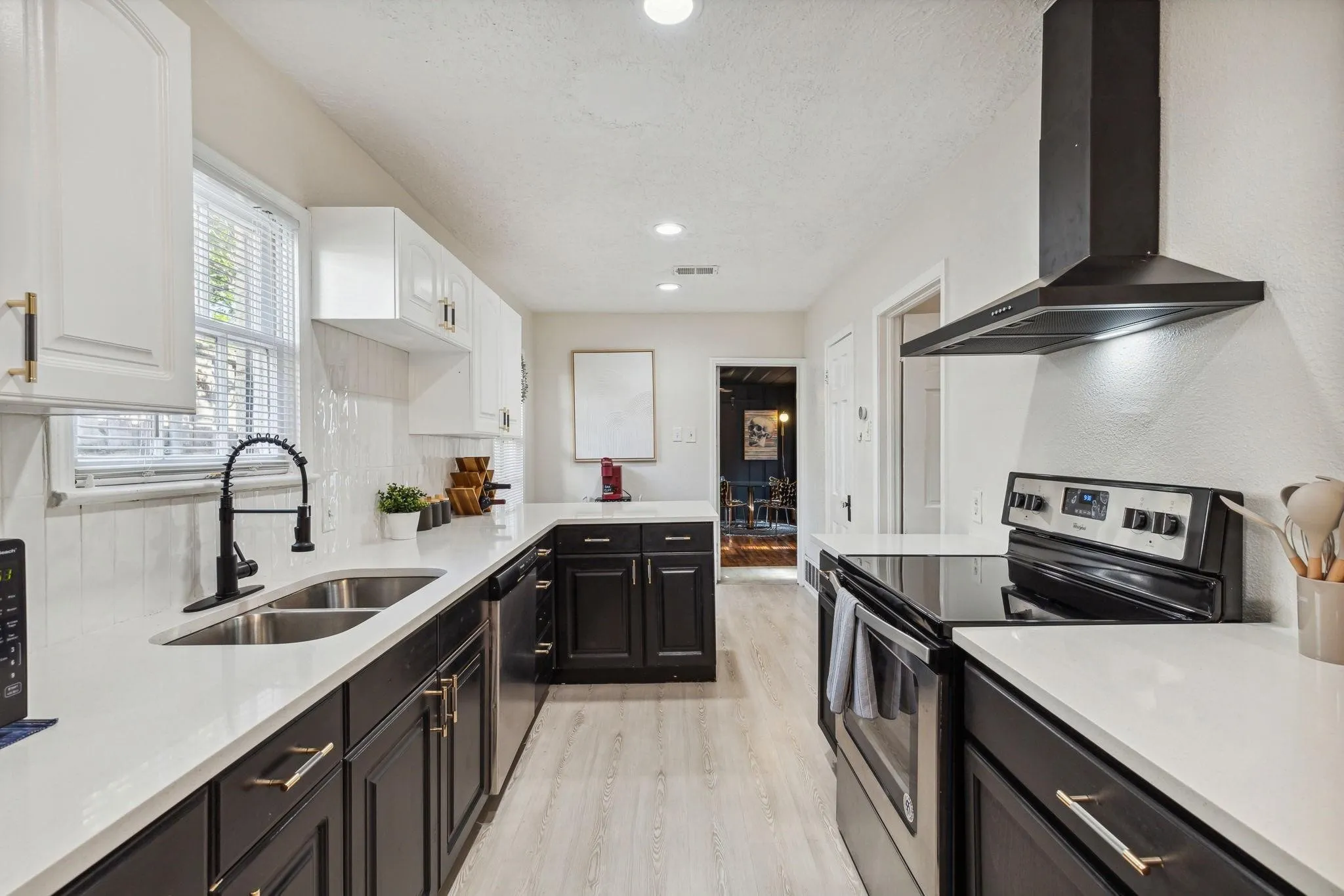 Galley kitchen with white upper cabinetry, dark lower cabinetry, stainless steel sink, black range, and black range hood