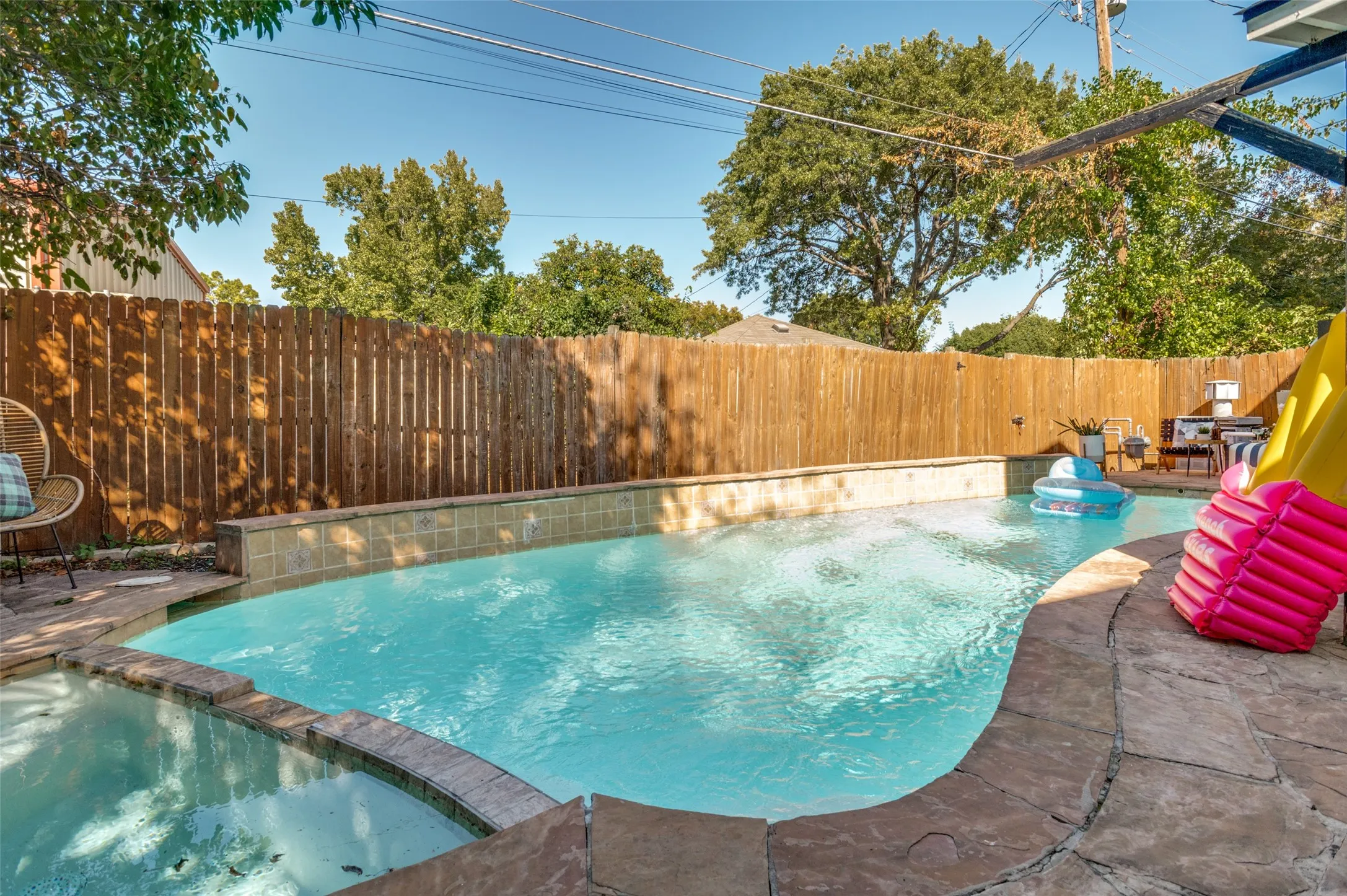 Private backyard featuring a swimming pool with integrated spa and stone coping, surrounded by a wood privacy fence