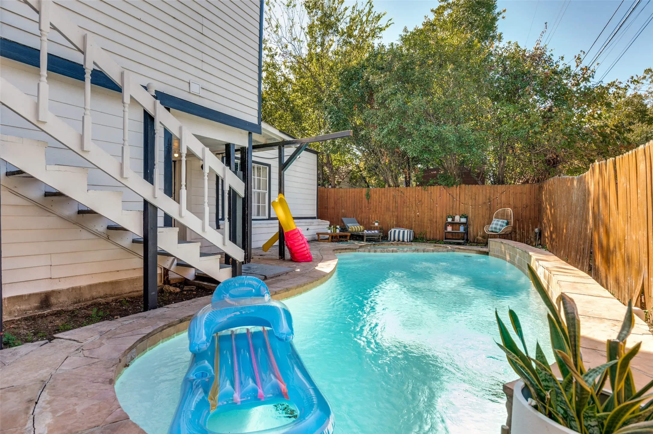 Curved swimming pool with stone coping and surrounding wood privacy fence
