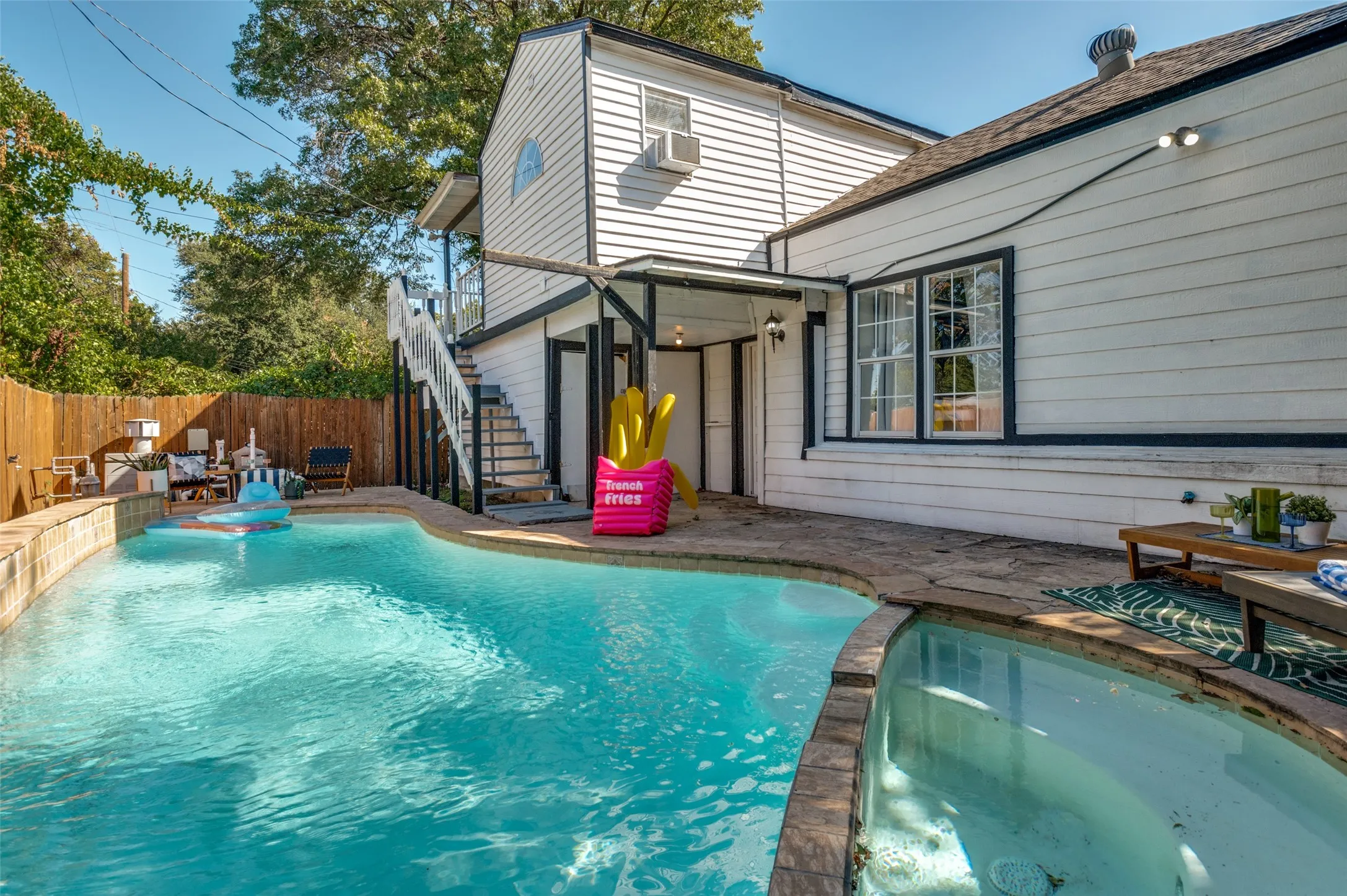 Curved swimming pool with integrated spa, stone coping, wood fencing, and multi-level exterior with an external staircase