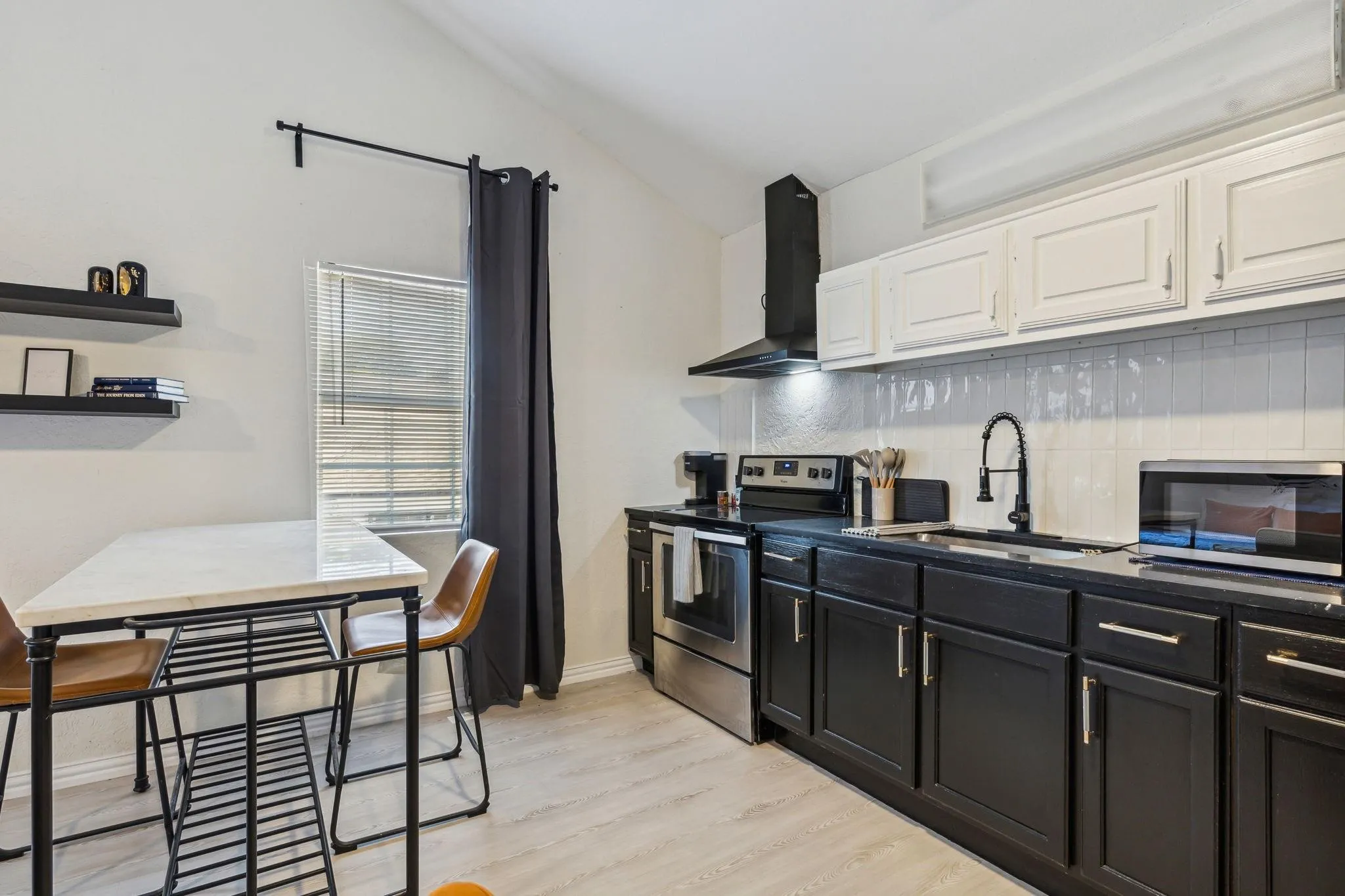 Vaulted ceiling, wood-finish flooring, white subway tile backsplash, matte black gooseneck faucet, and stainless steel appliances