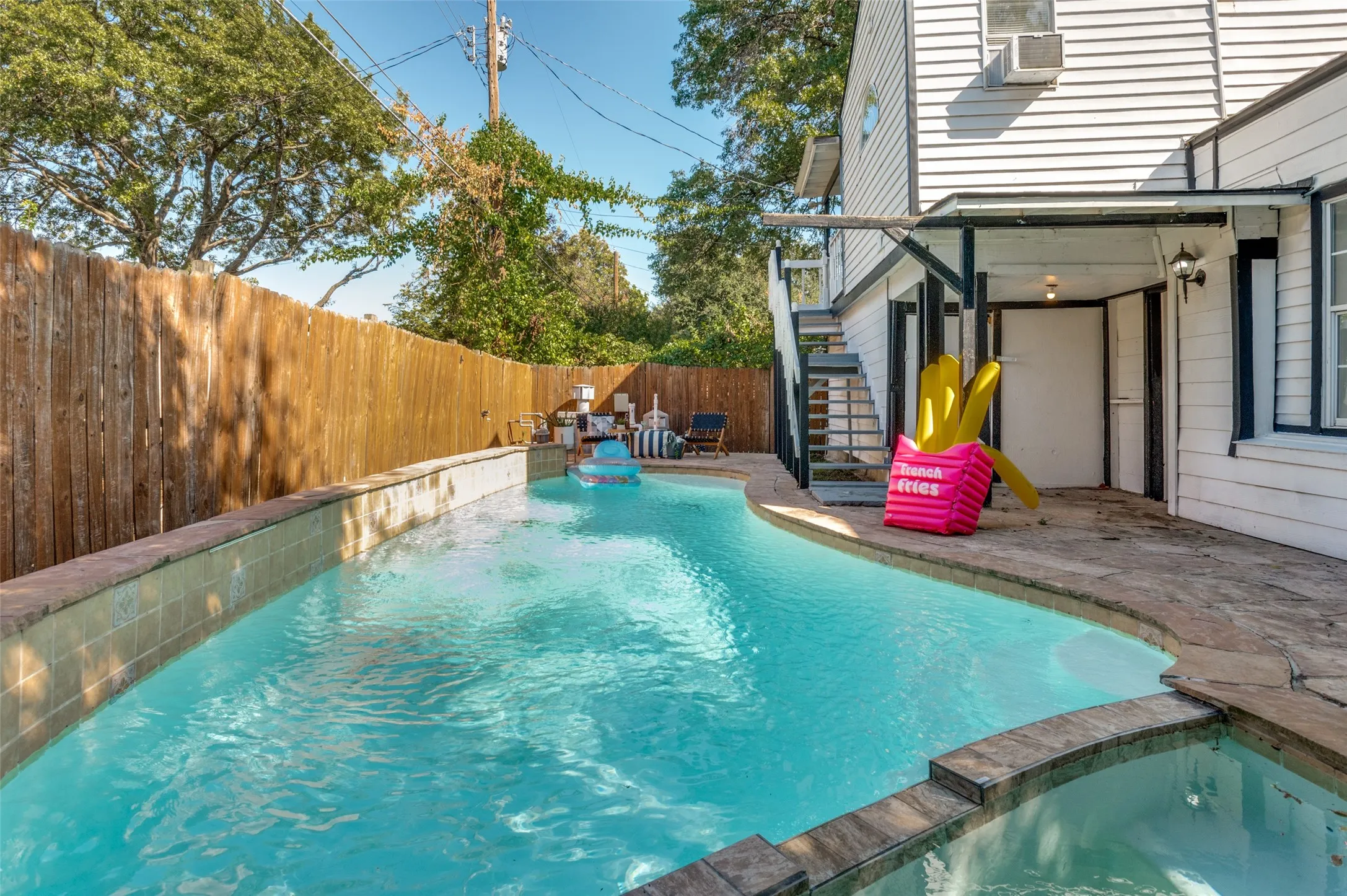 Custom-shaped swimming pool with an integrated spa, bordered by flagstone coping and a wood privacy fence