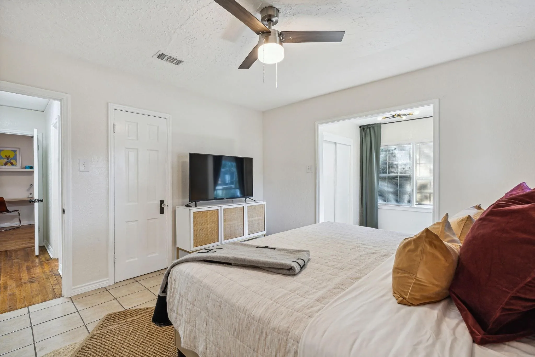 White walls, ceiling fan with light fixture, tile flooring, and a window with curtain rod and drapes