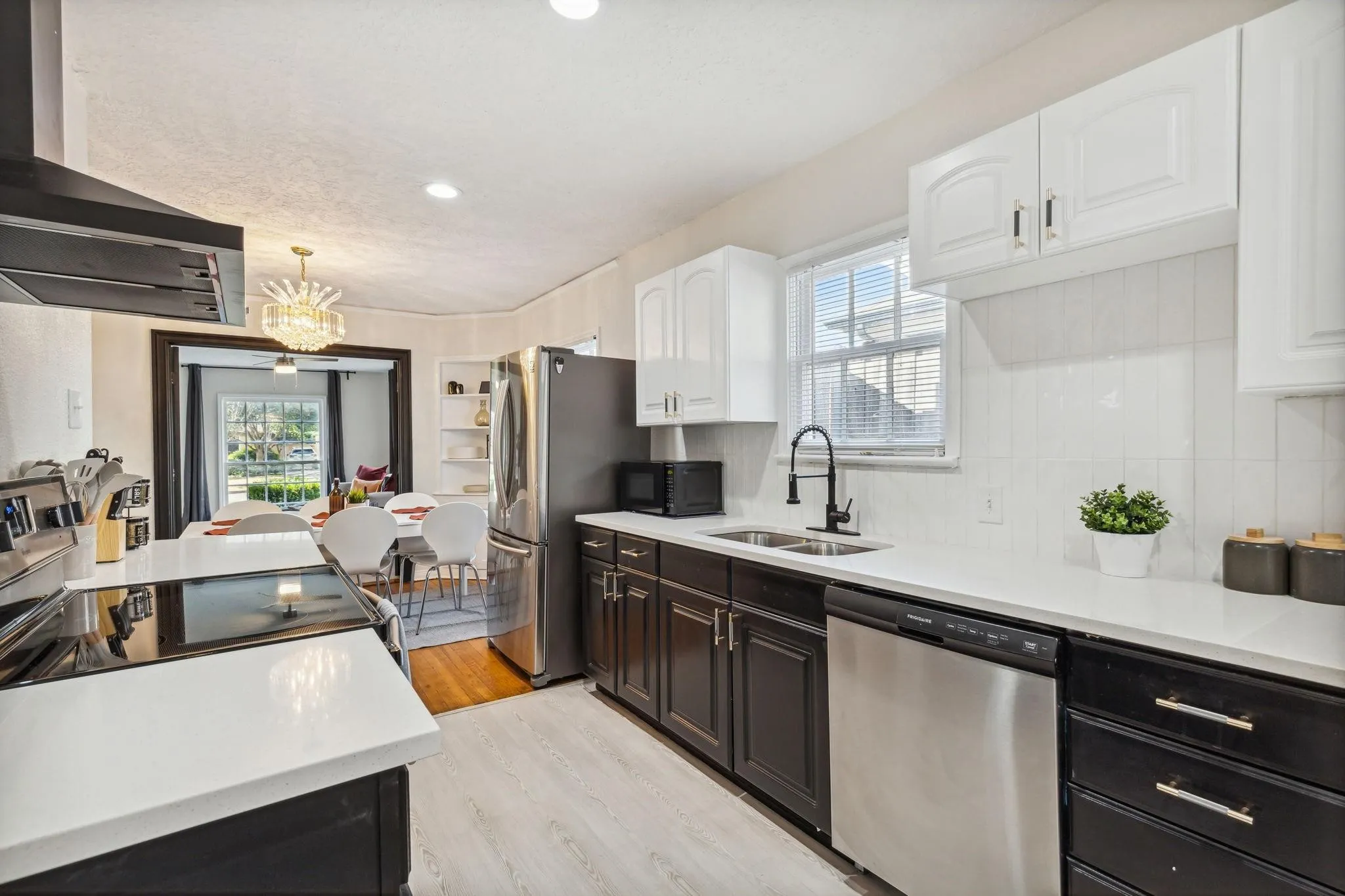 Kitchen featuring white upper cabinetry, dark lower cabinetry, stainless steel appliances, a double basin sink with a matte black faucet, and light wood-finish flooring
