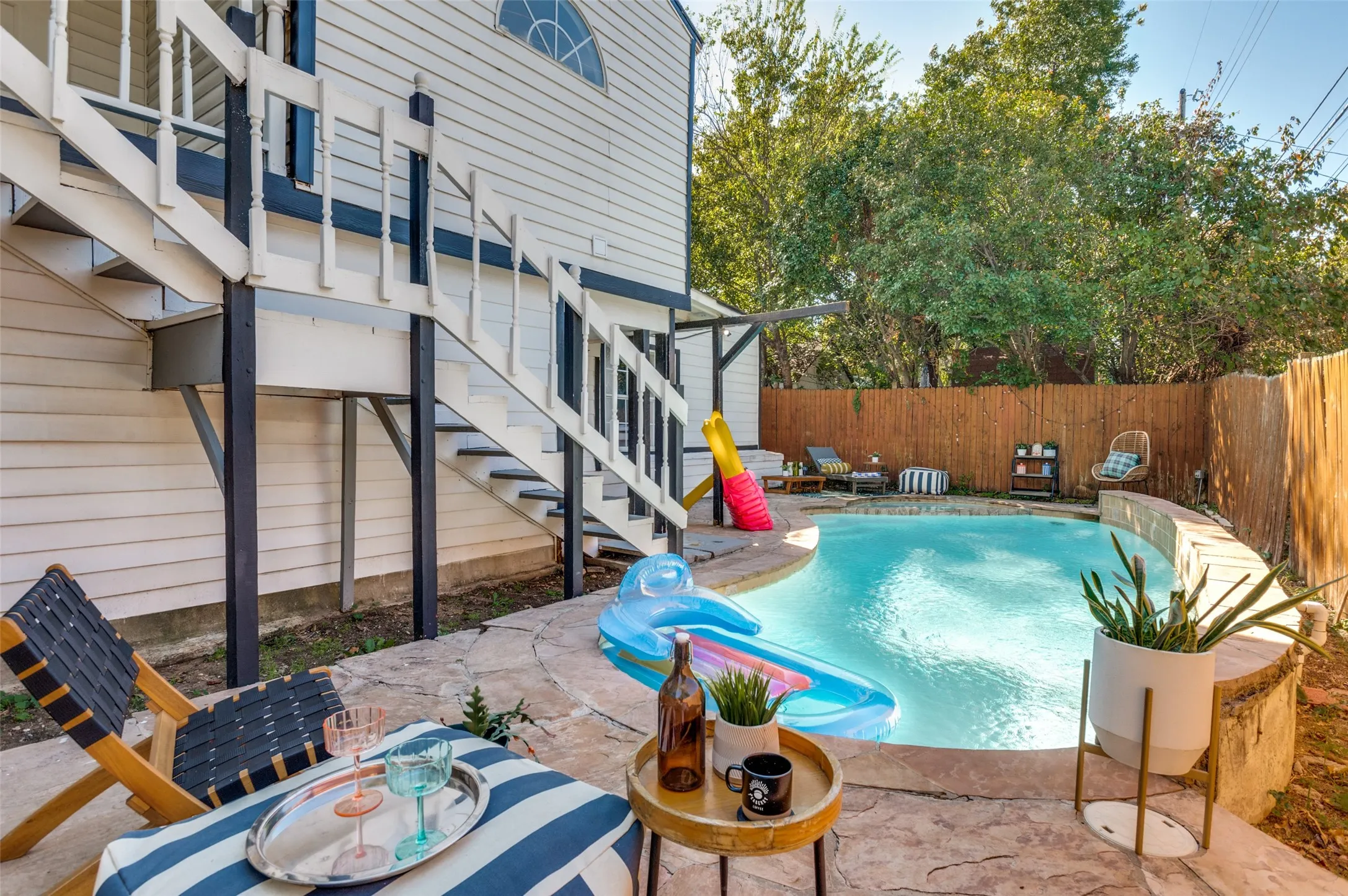 Exterior staircase with white railings, private swimming pool, flagstone patio, wood fence, and mature trees