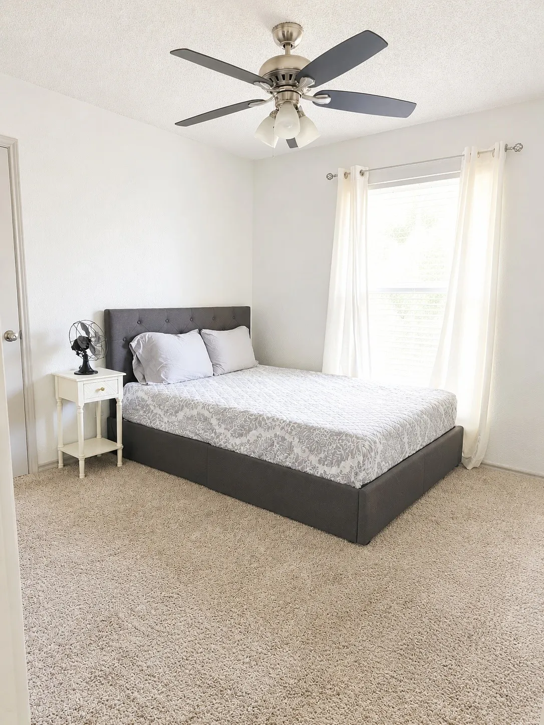Neutral-toned wall-to-wall carpeting, window with blinds and sheer curtains, and a ceiling fan with integrated lighting