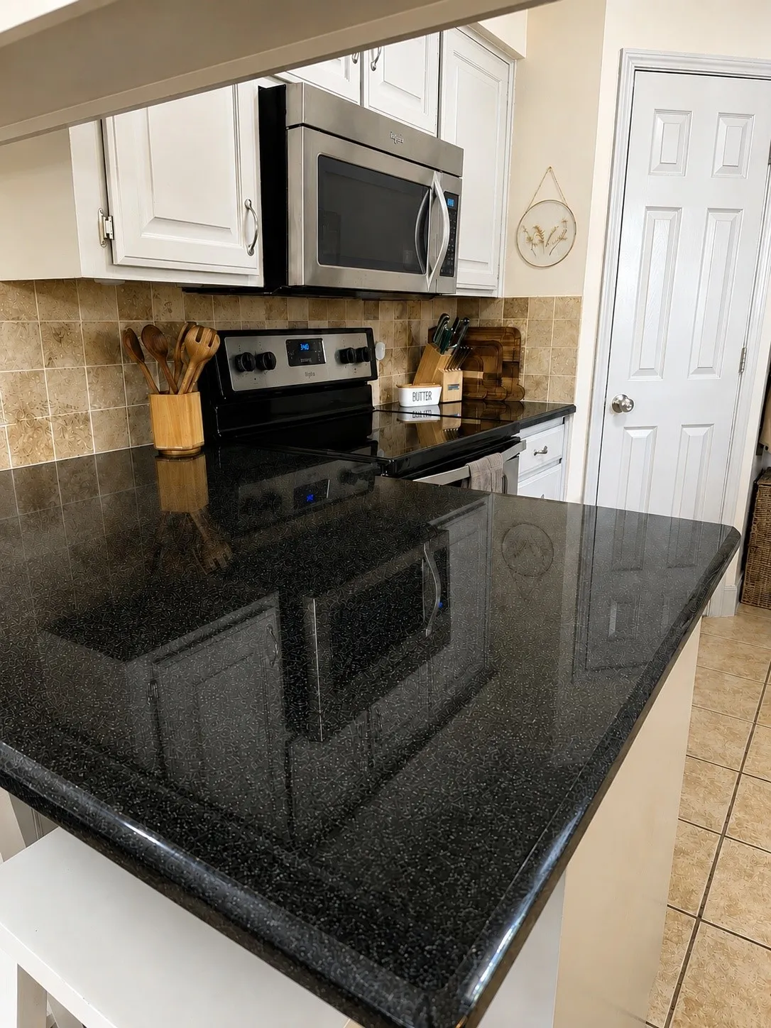 Black speckled countertop, stainless steel microwave, white cabinetry, tile backsplash, and built-in electric range