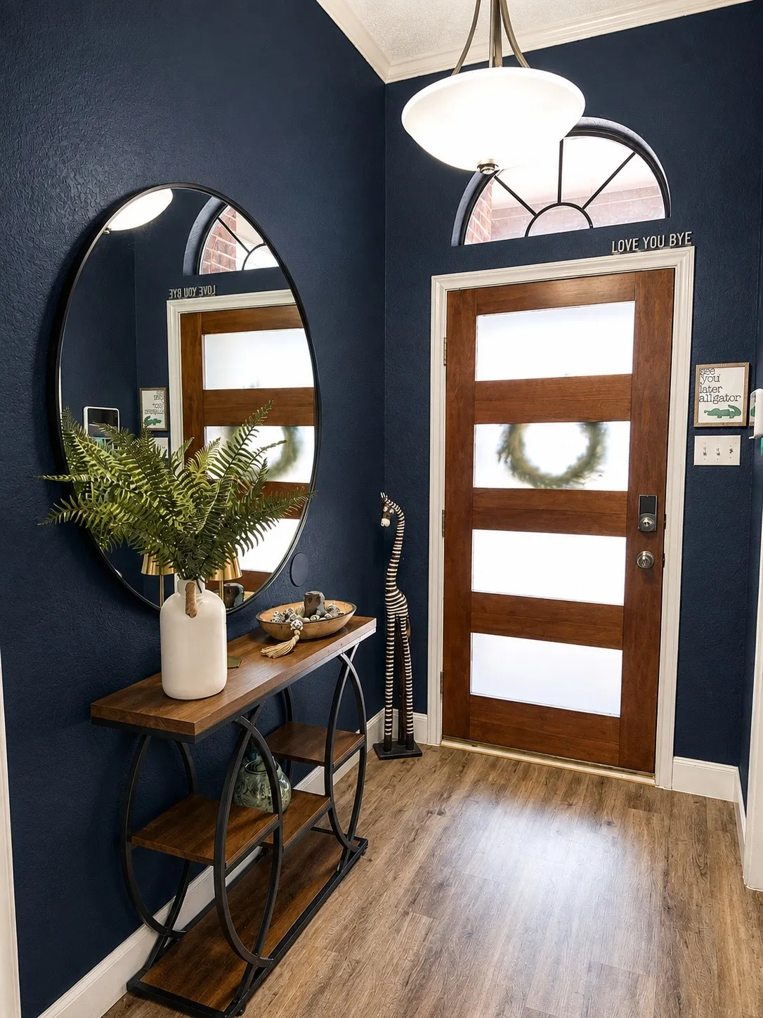 Warm wood-finish flooring, a solid wood entry door with frosted panels, and an arched transom window