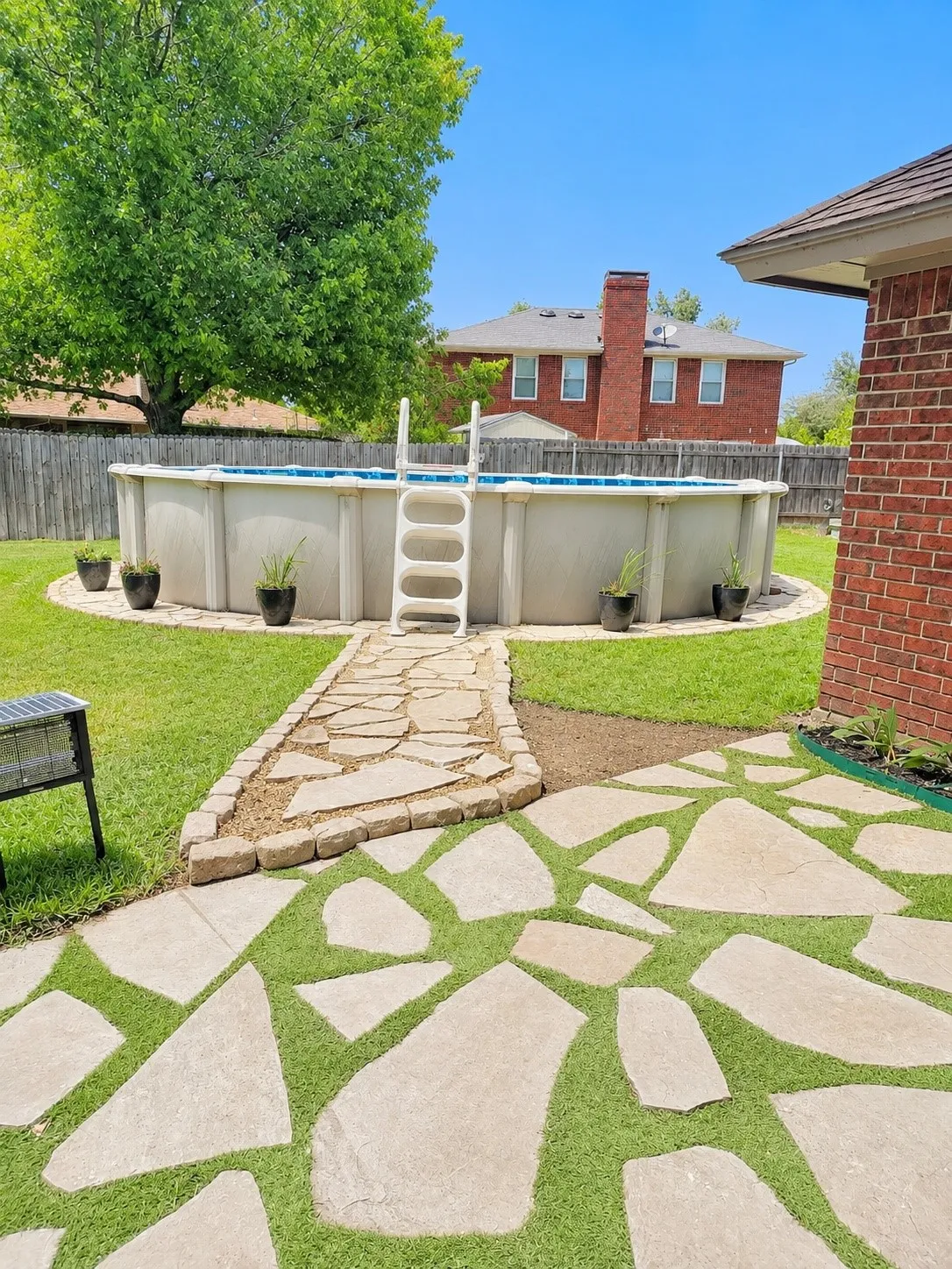 Expansive backyard featuring a stone patio, flagstone pathway, above-ground pool, and a wooden privacy fence