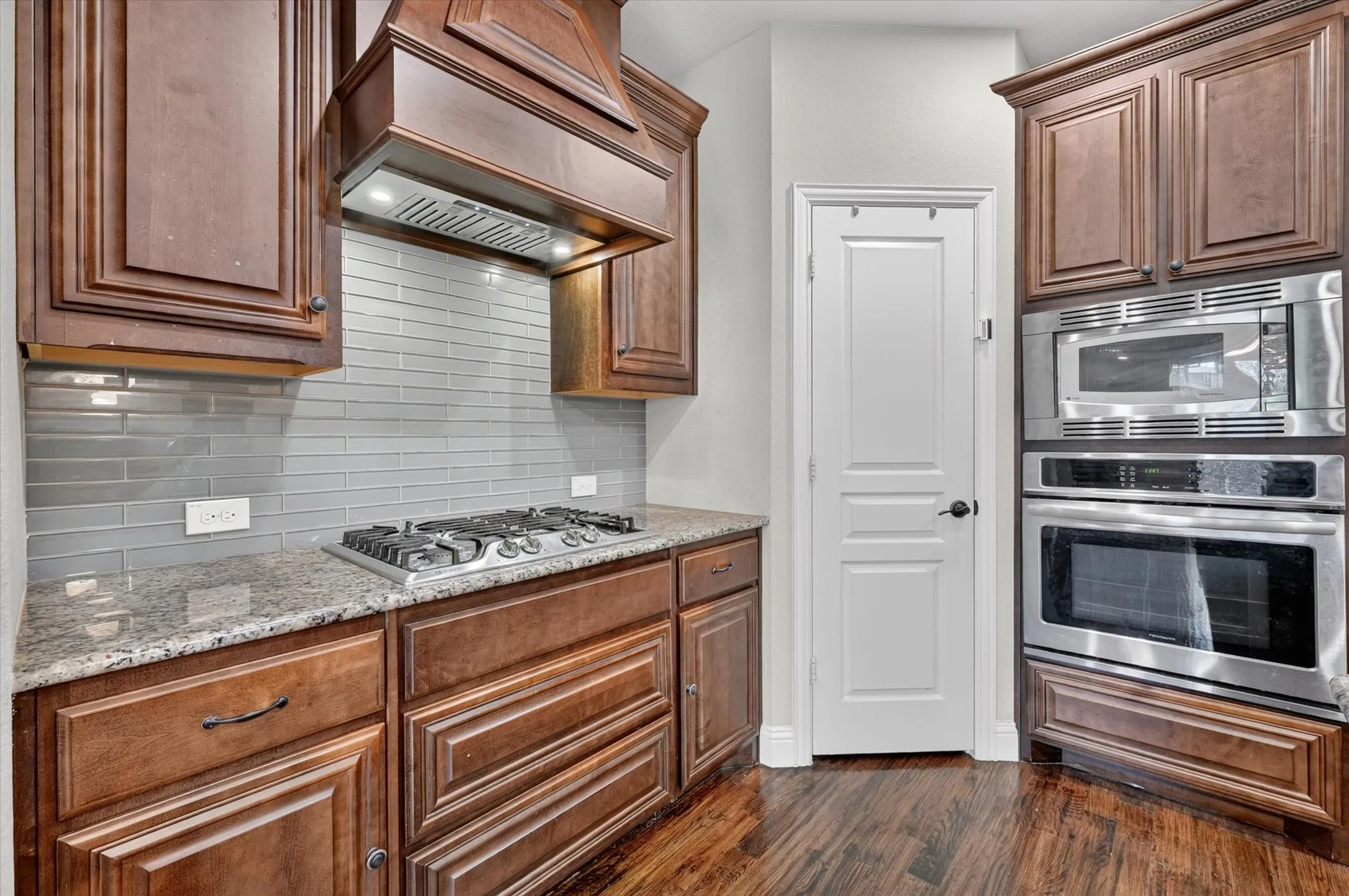 Wood-finish flooring, dark wood cabinetry, stainless steel oven, stainless steel microwave, and a gas cooktop