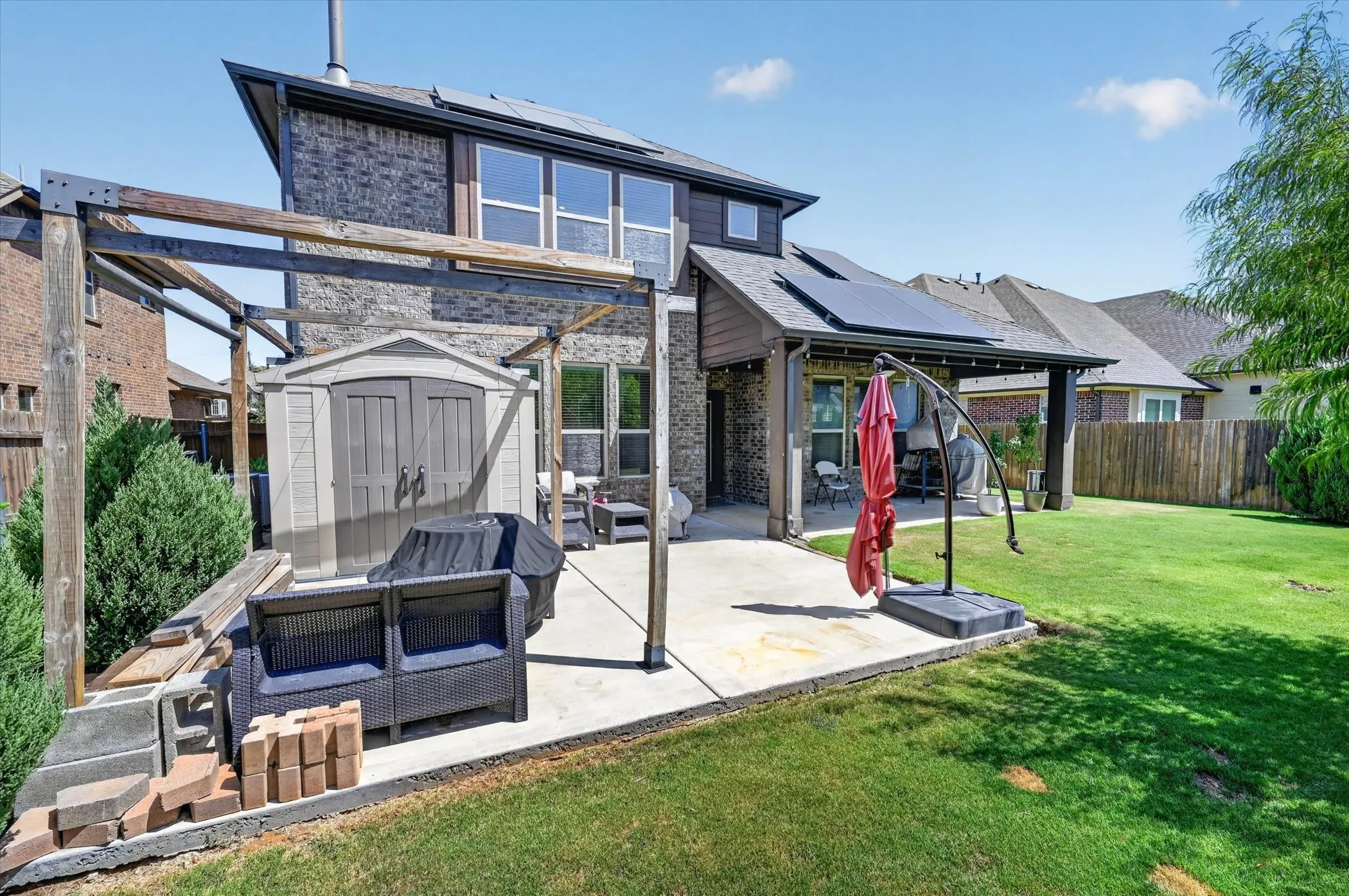 Expansive backyard with a concrete patio, wood pergola frame, and a storage shed