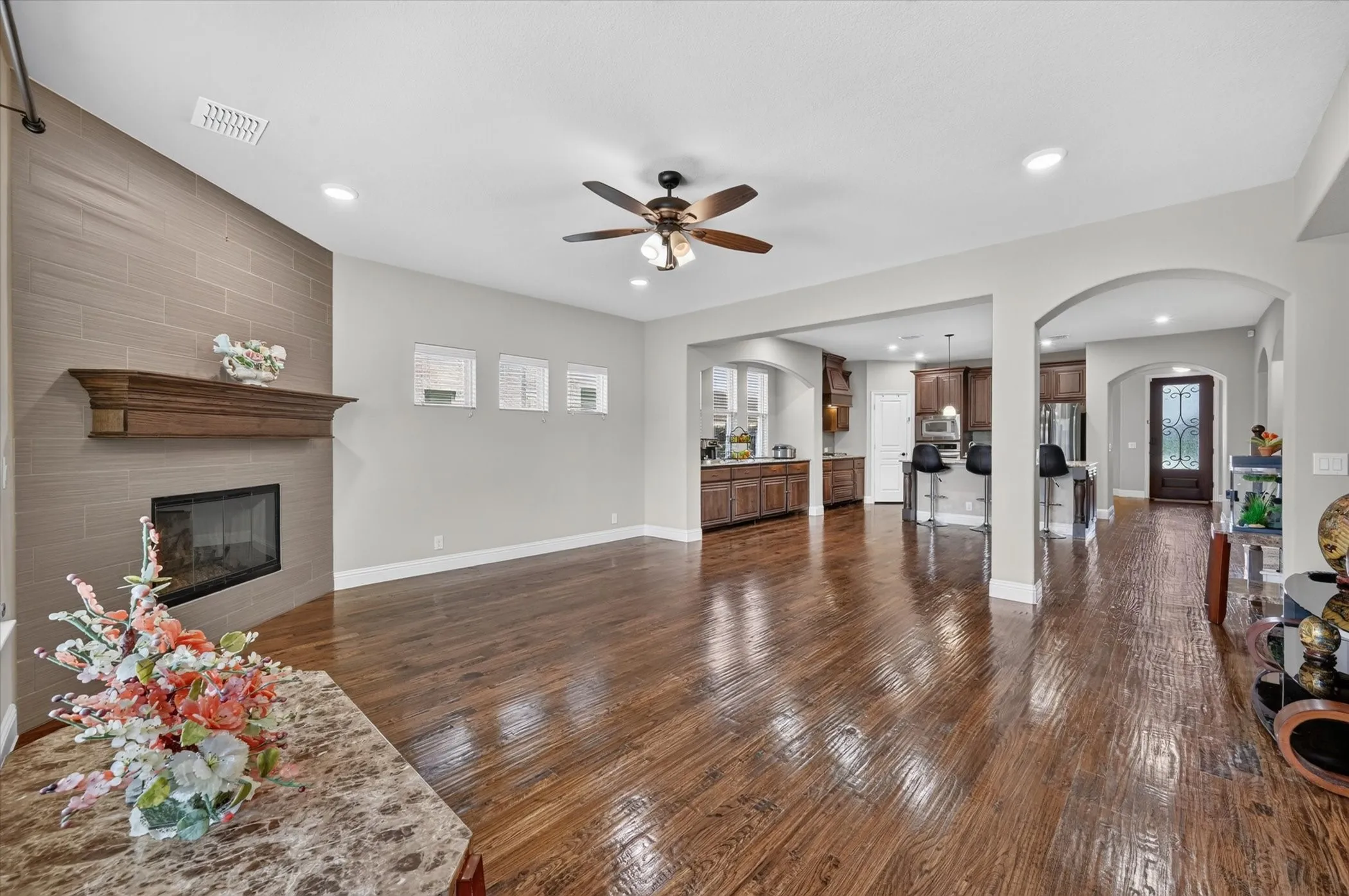 Open-concept living space featuring wood-finish flooring, a tiled fireplace with wood mantel, recessed lighting, and a ceiling fan