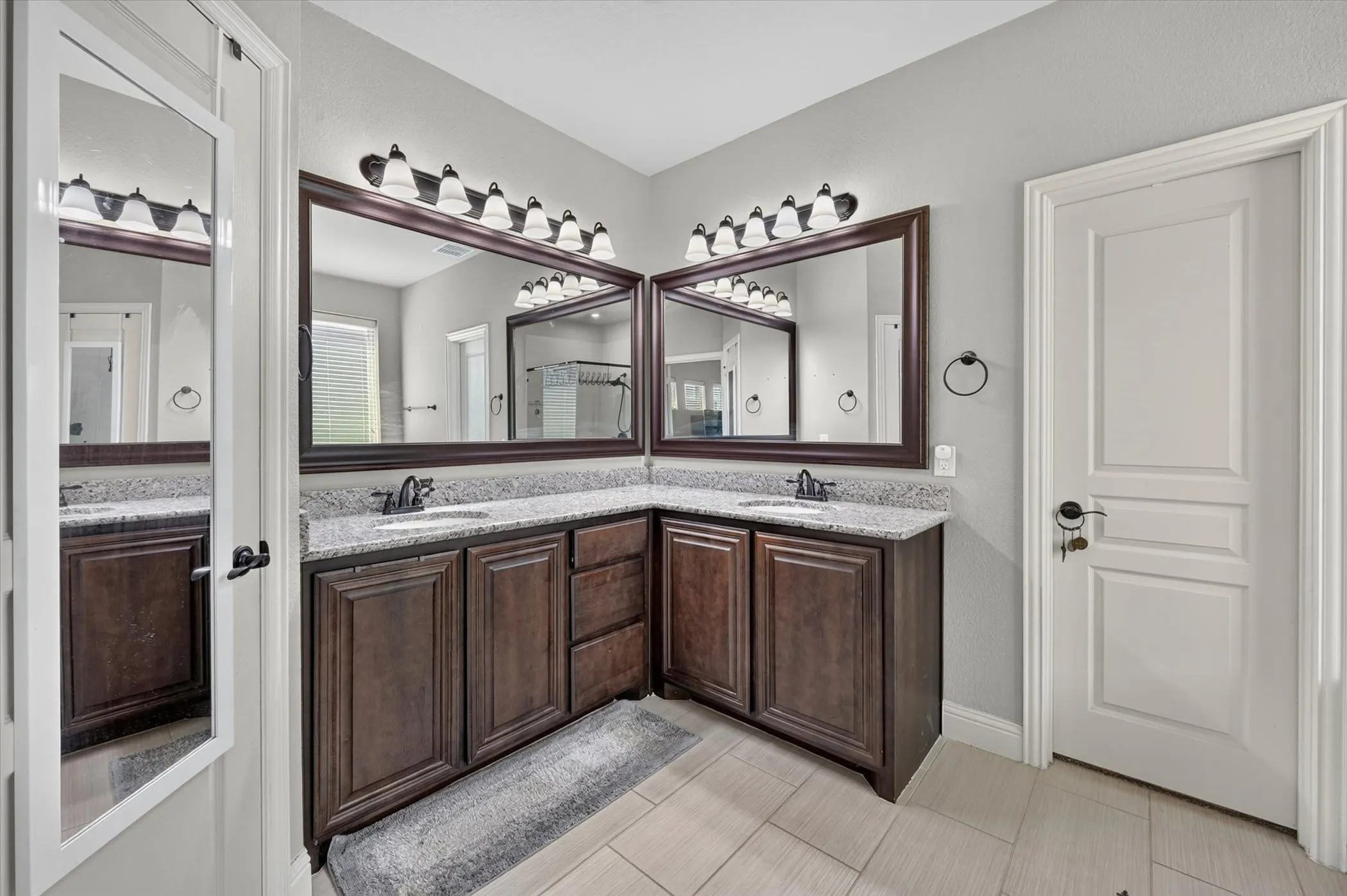 Dual wood-finish vanities with light-colored countertops, framed mirrors, and tile flooring