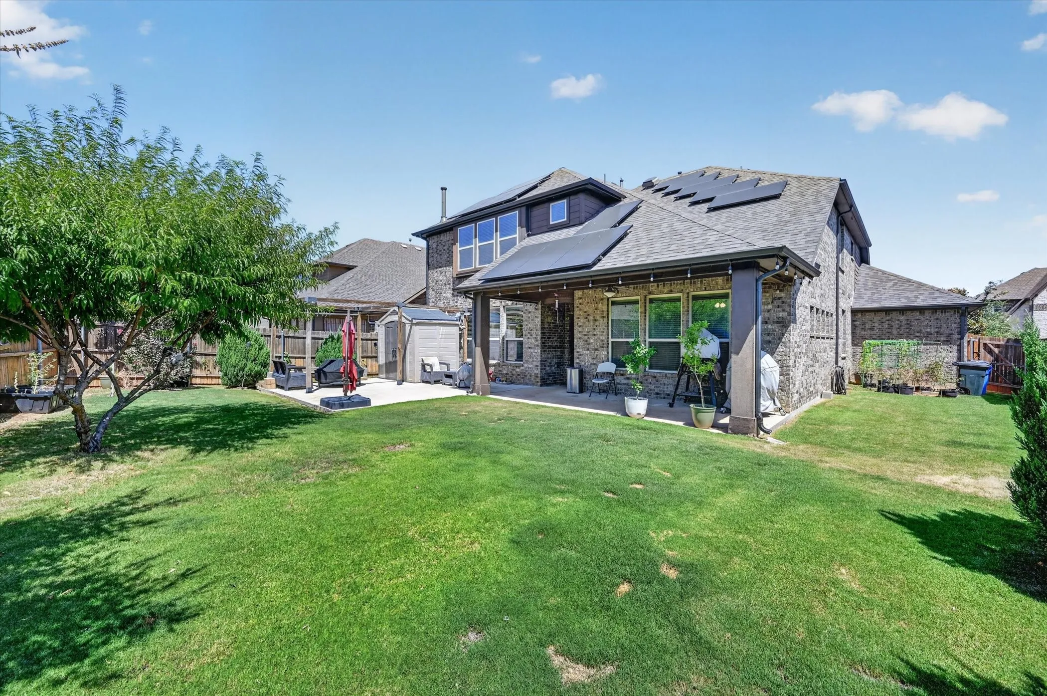 Expansive backyard featuring a stone and brick exterior, covered patio, solar panels, and a concrete patio surface