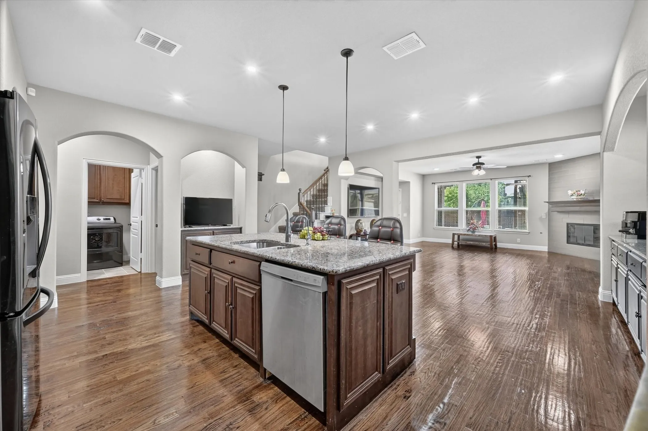 Kitchen island with granite countertop, integrated stainless steel dishwasher, and under-mount sink, complemented by wood-finish flooring