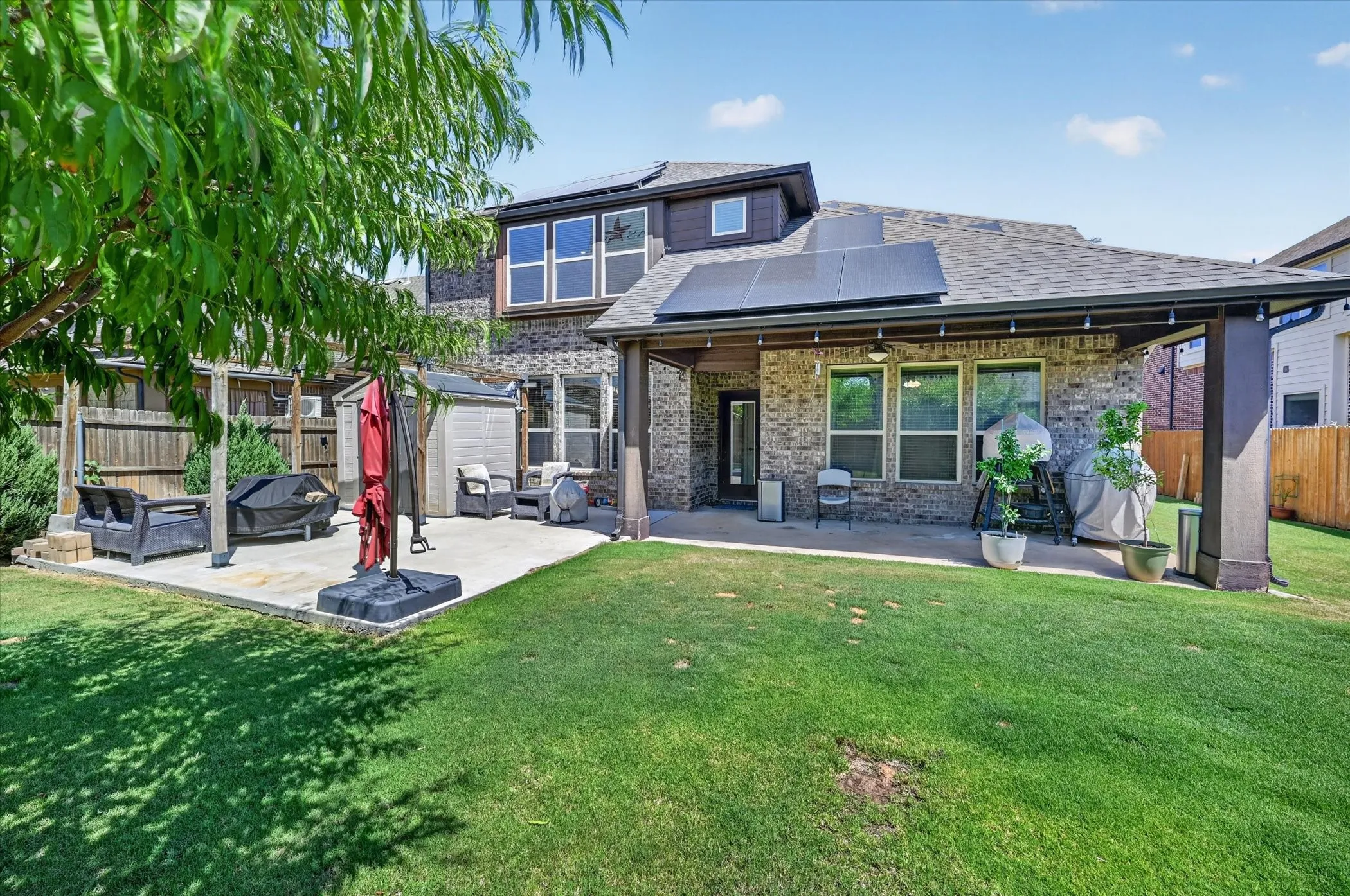 Expansive backyard featuring a covered patio, additional concrete patio space, wood fence, and solar panels