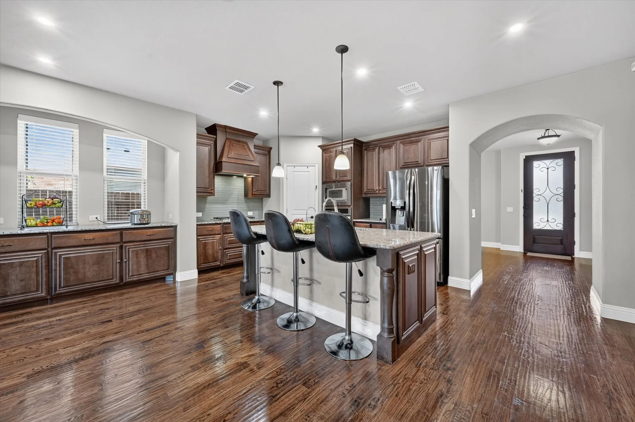Spacious kitchen featuring rich wood cabinetry, stone countertops, a large island with seating, stainless steel appliances, and wood-finish flooring