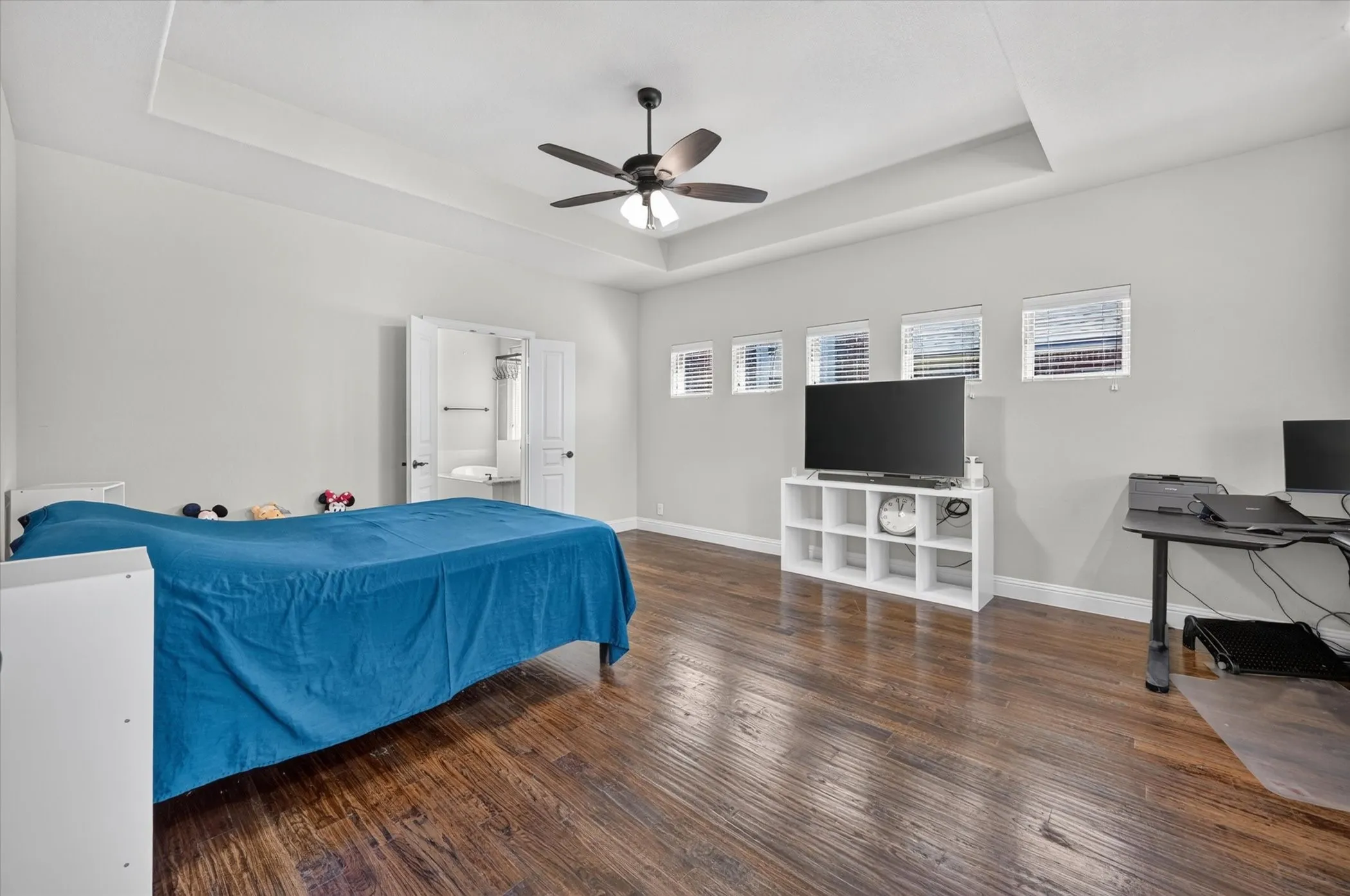 Tray ceiling with a ceiling fan, dark wood-finish flooring, and multiple windows