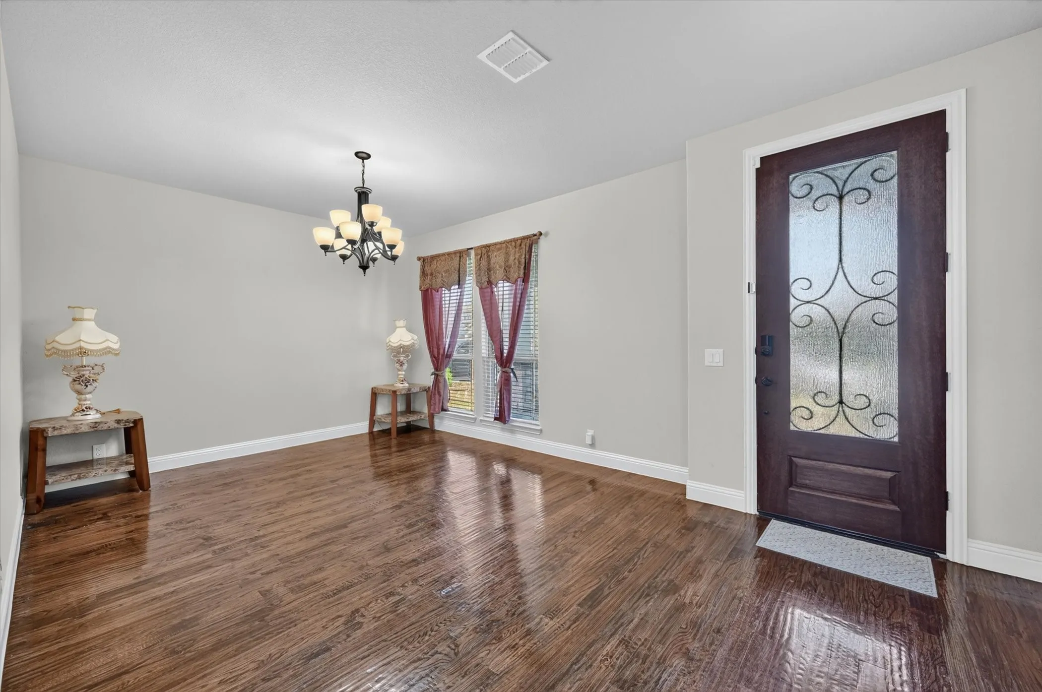 Dark wood-finish flooring, a decorative glass-paneled entry door, and a multi-arm chandelier