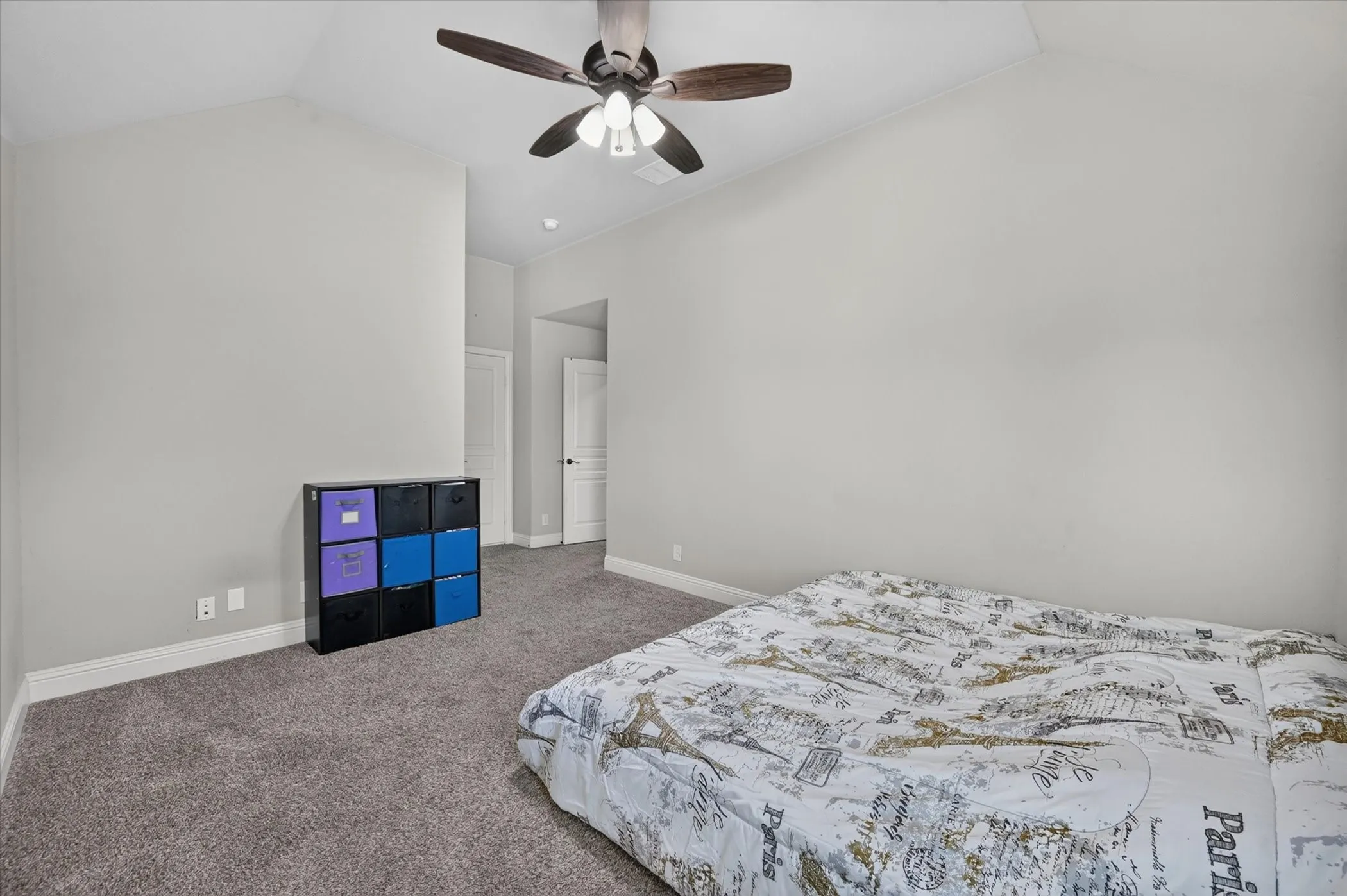 Vaulted ceiling, light gray wall paint, dark wood-finish ceiling fan with integrated lighting, gray carpeting, and white trim