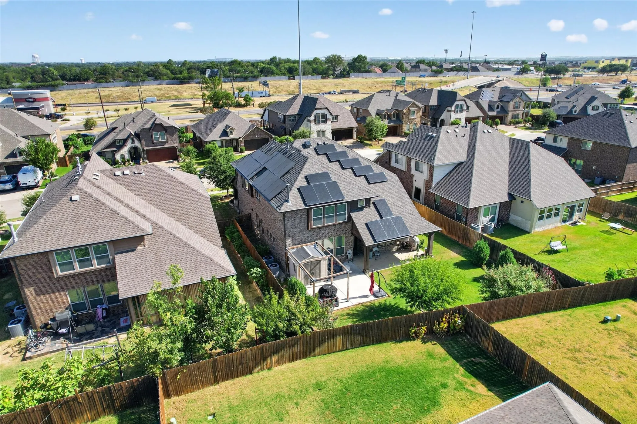 Brick-clad residence with a shingled roof, featuring multiple solar panels and a covered patio