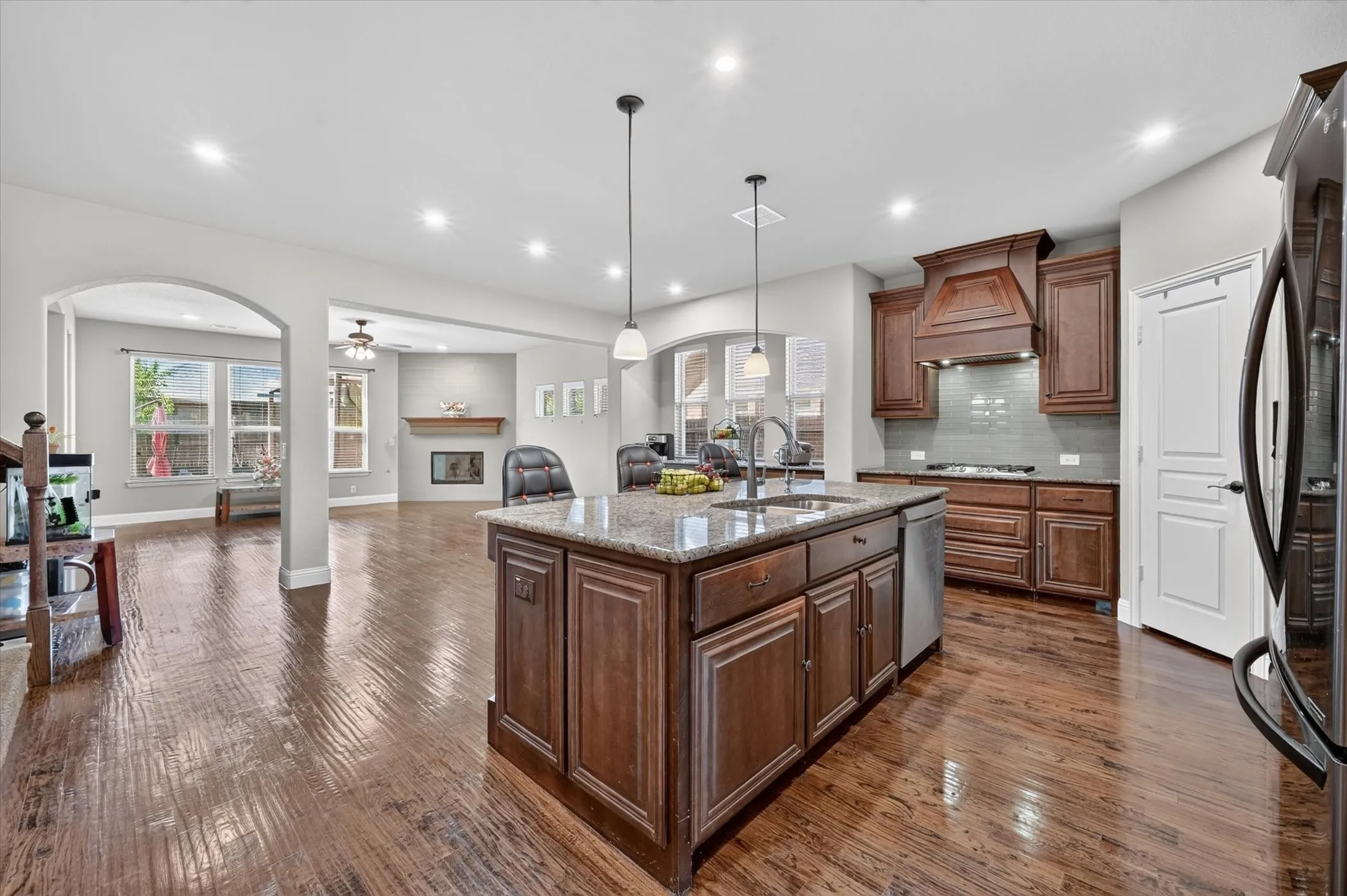Kitchen island with granite countertops, rich wood cabinetry, stainless steel appliances, and wood-finish flooring