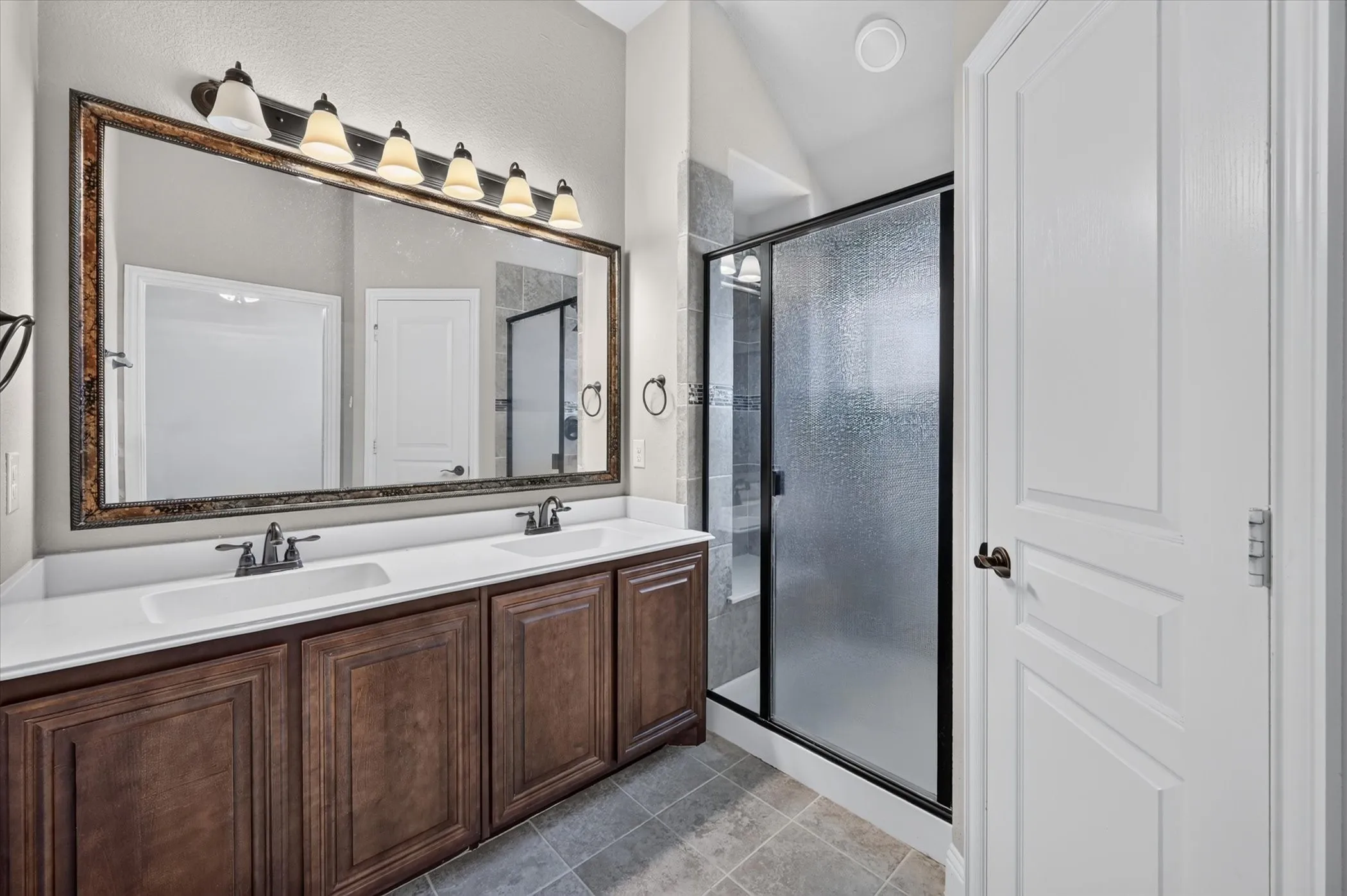 Upstairs Primary Bathroom 2 Dual vanity with integrated sinks, framed mirror, six-light fixture, tiled flooring, and a glass-enclosed shower