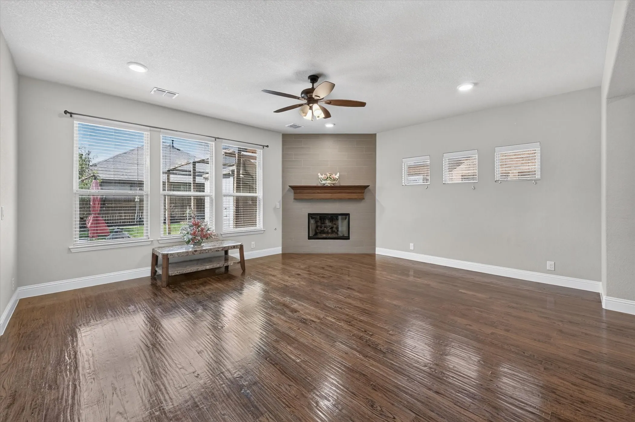 Spacious living area featuring wood-finish flooring, a corner fireplace with a wood mantle and tile surround, recessed lighting, and a ceiling fan