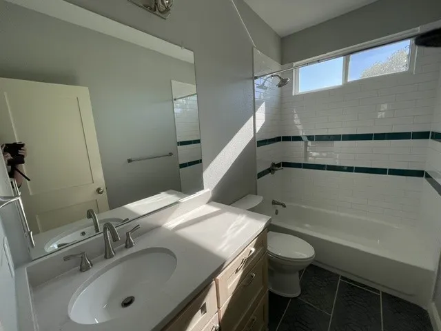 Vanity with an integrated sink and brushed nickel faucet, large wall mirror, subway tile shower surround with decorative accent bands, and a window above the shower