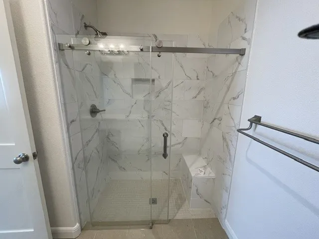 Walk-in shower with a glass enclosure, white marble-look tile, built-in bench, and a recessed niche