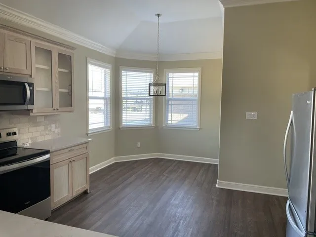 Bay window with multiple windows, wood-finish flooring, recessed lighting, crown molding, and stainless steel appliances