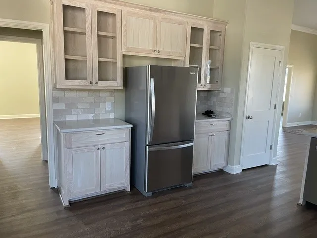 Stainless steel refrigerator, wood-finish flooring, light-toned cabinetry, subway tile backsplash, and light-toned countertops