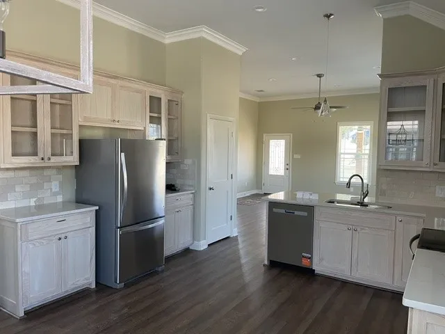Kitchen featuring light-finish cabinetry, stainless steel appliances, solid surface countertops, a tile backsplash, and wood-finish flooring