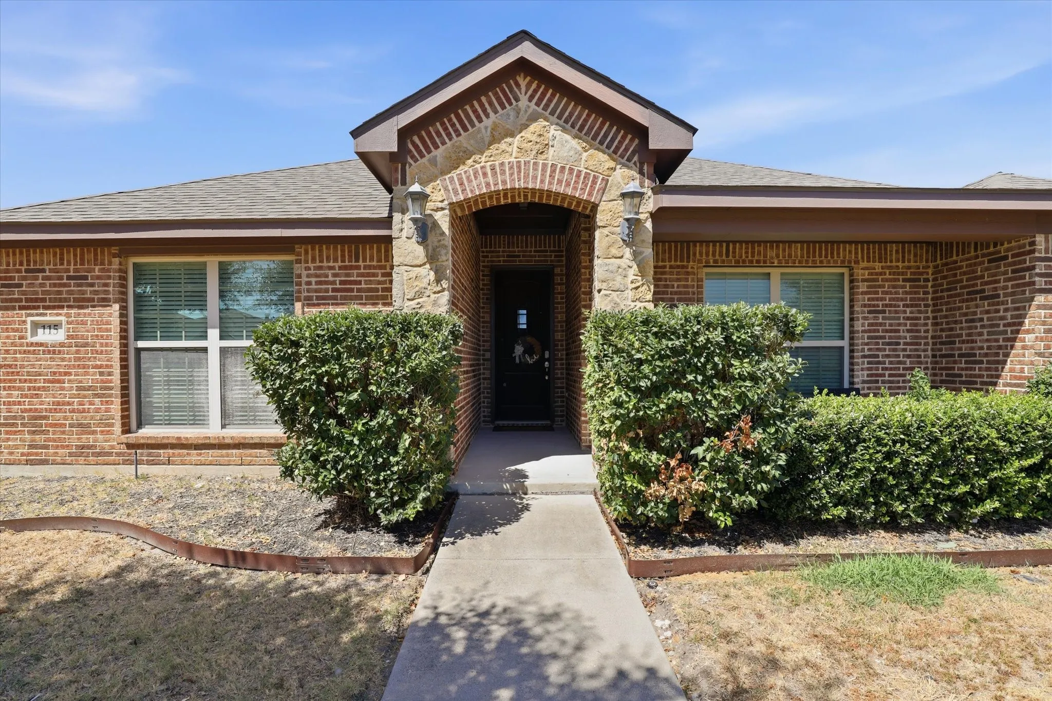 Brick and stone exterior with an arched entryway, covered porch, and concrete walkway