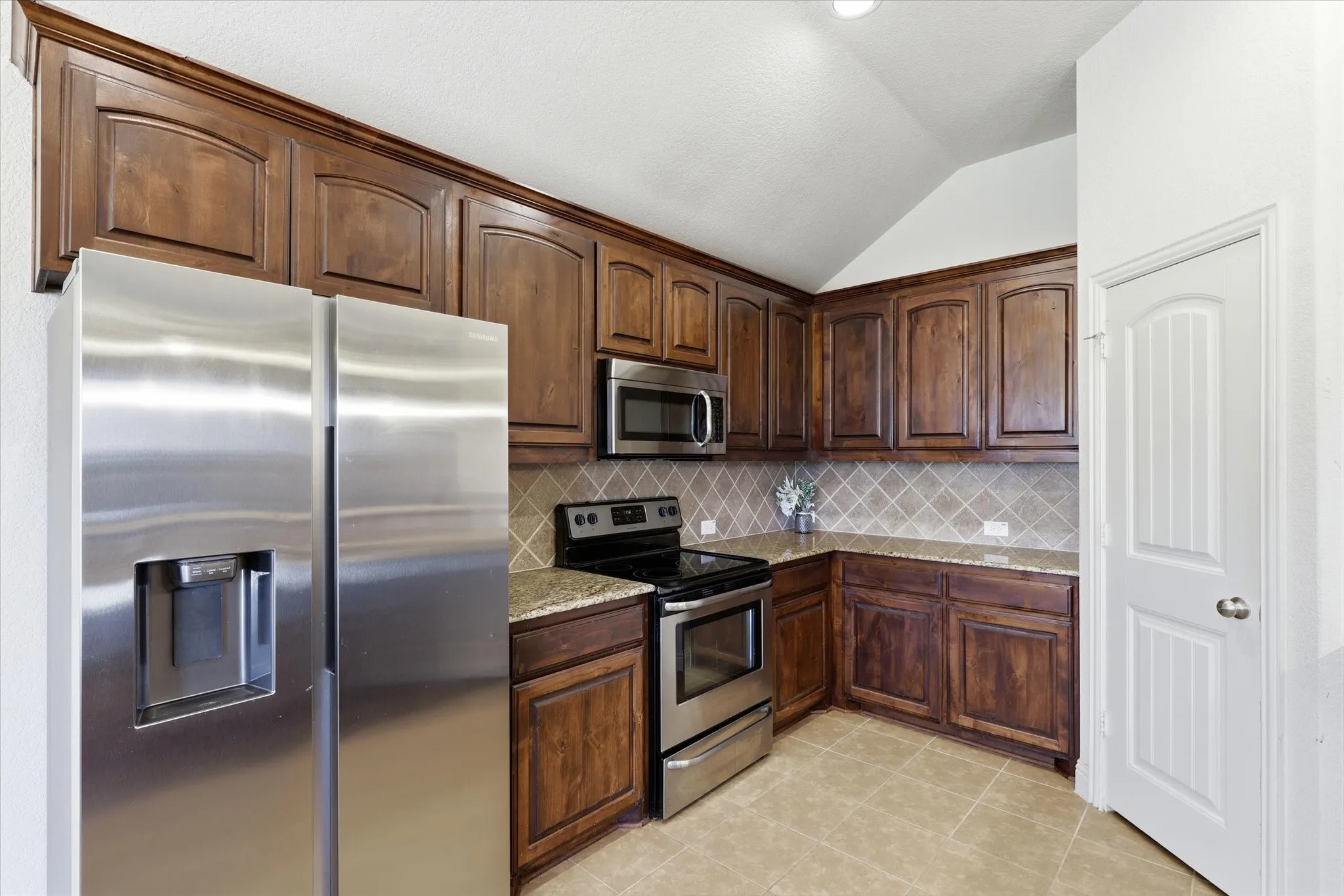 Stainless steel appliances, wood-finish cabinetry, tile flooring, stone countertops, and a tile backsplash