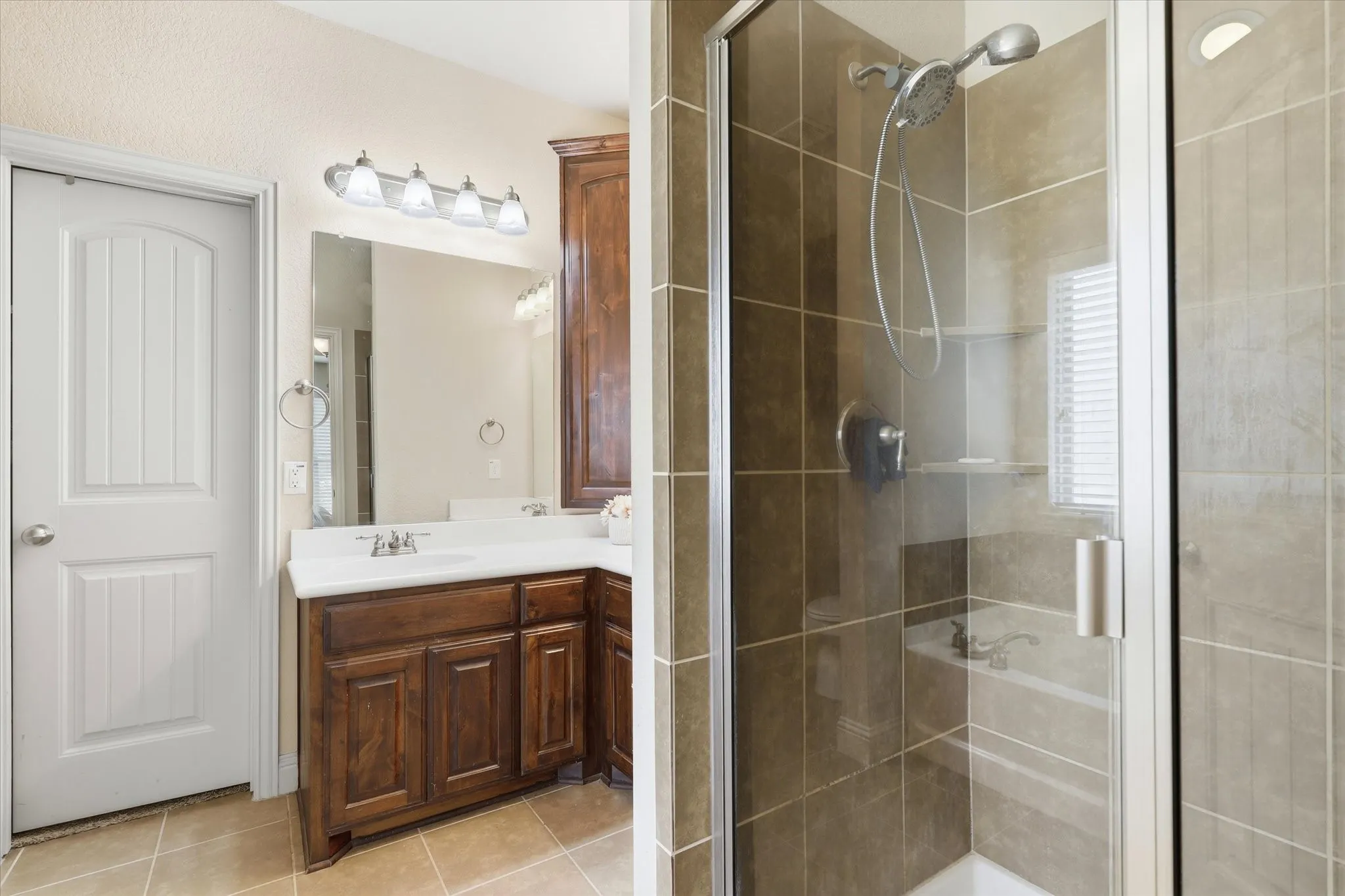 Bathroom featuring a wood-finish vanity with a white countertop, a framed mirror, and a glass-enclosed shower with tiled walls and a built-in shelf