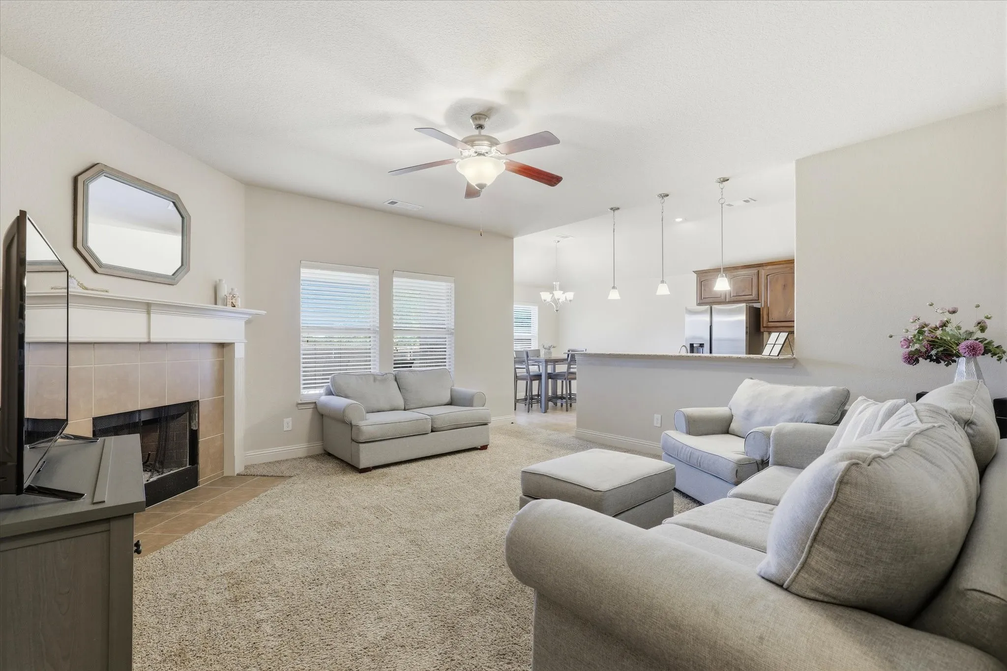 Living area featuring a tiled fireplace with mantel, ceiling fan, and two windows with blinds