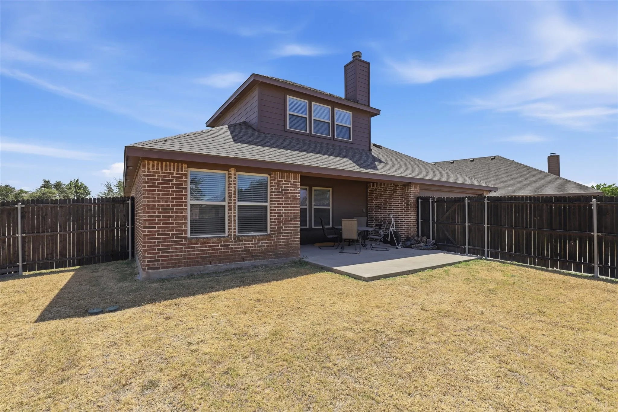 Rear exterior with brick and siding facade, concrete patio, and a privacy fence