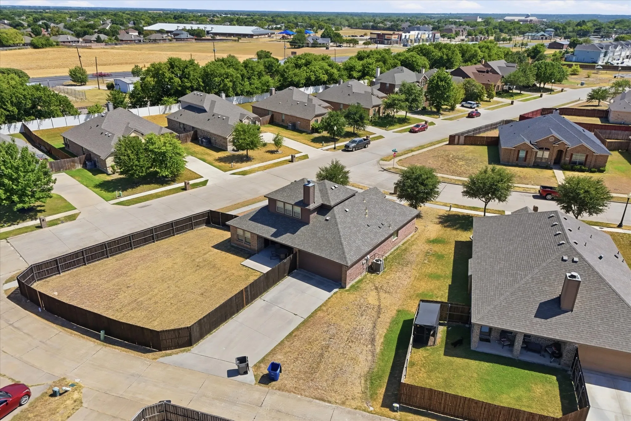 Brick exterior residence with an attached garage, featuring a dark shingle roof and a fenced backyard