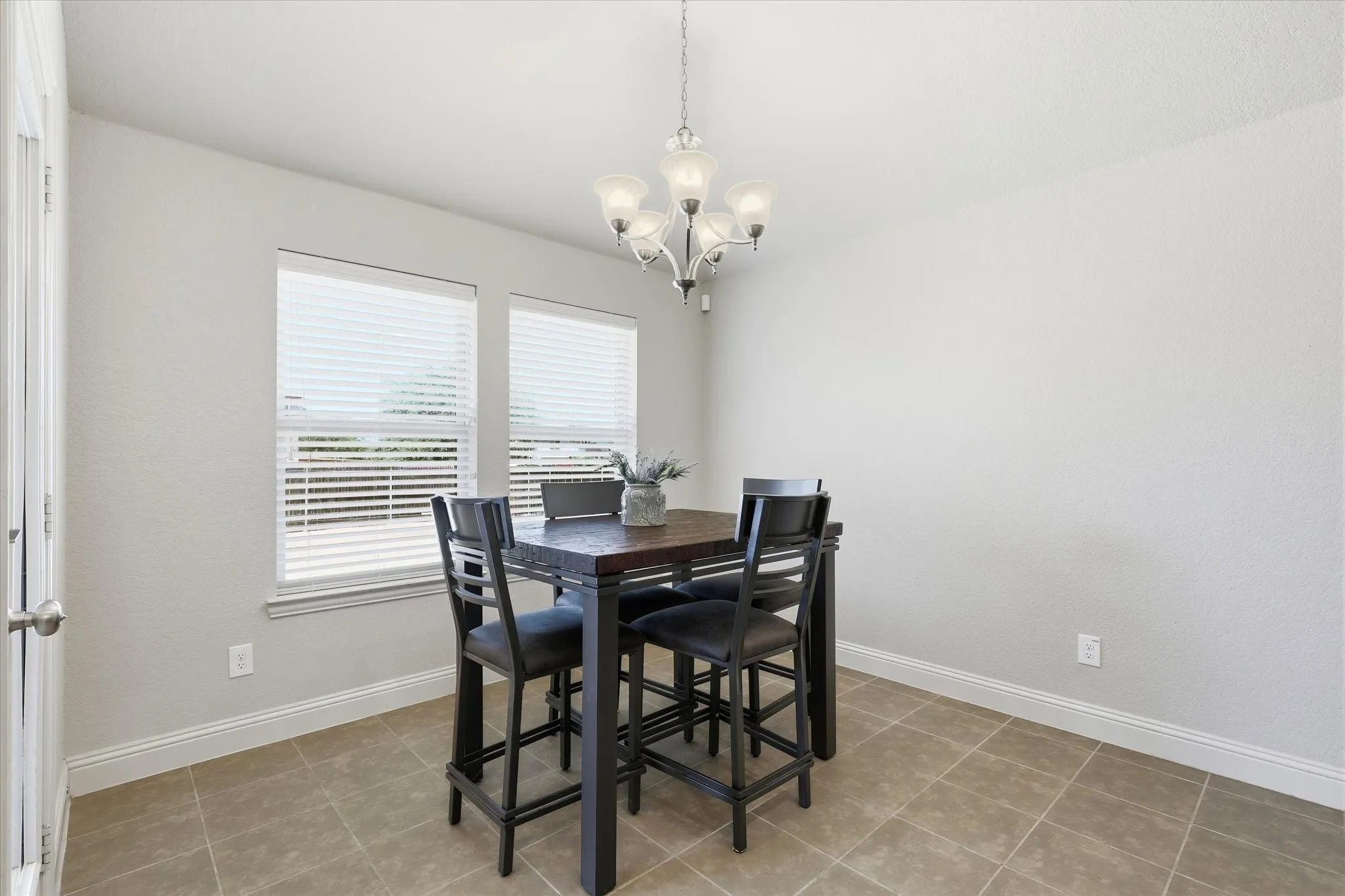Recessed dining area featuring tile flooring, two windows with blinds, and an attached five-light chandelier