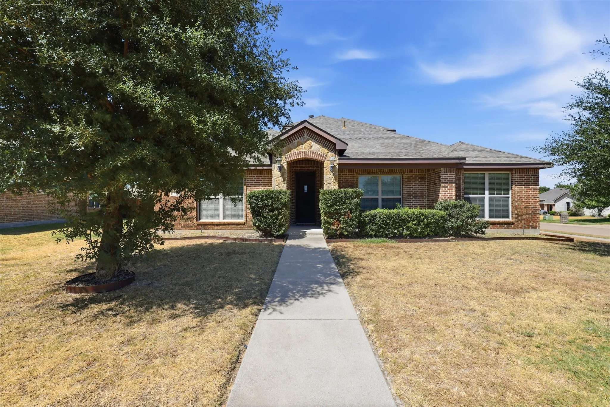 Brick exterior, gabled roof, mature tree, established shrubbery, concrete walkway