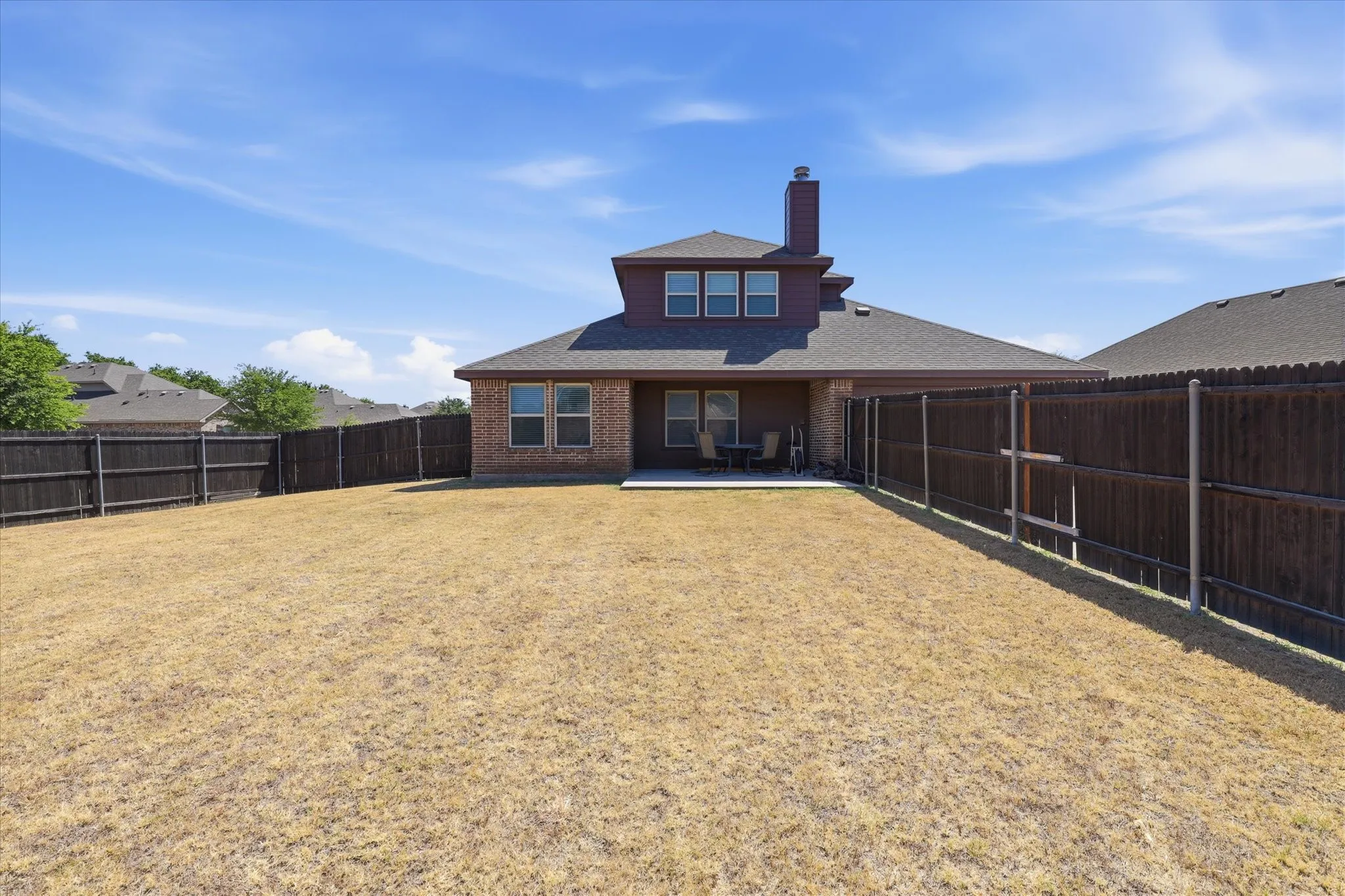 Expansive fenced backyard with a concrete patio, brick exterior, and multi-pane windows