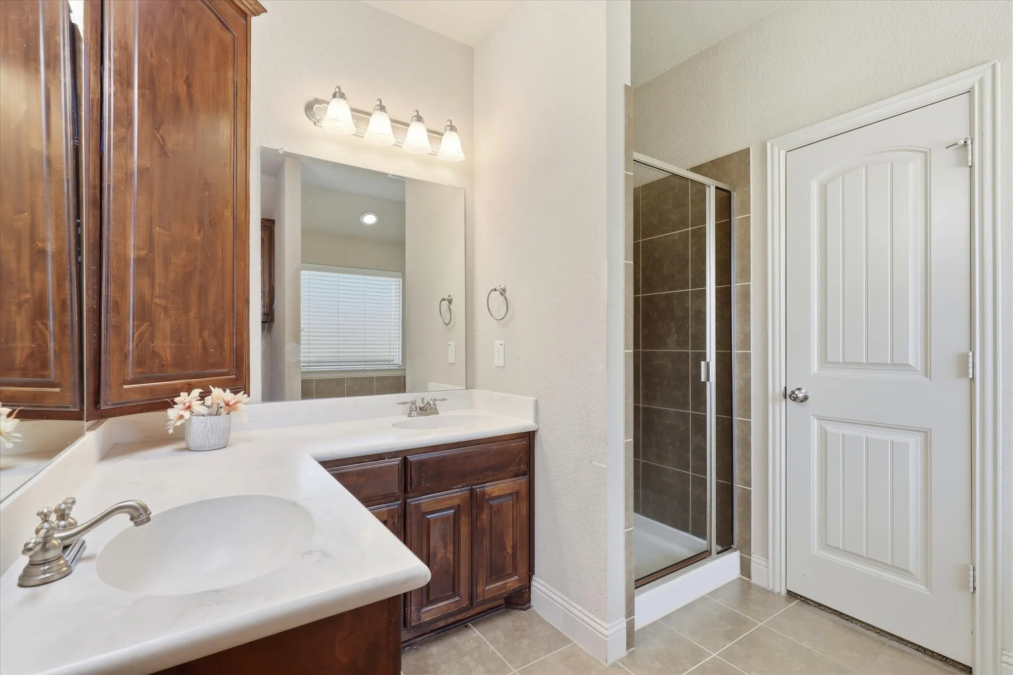 Dual vanity with integrated sinks, wood-finish cabinetry, frameless glass shower enclosure, and tiled flooring