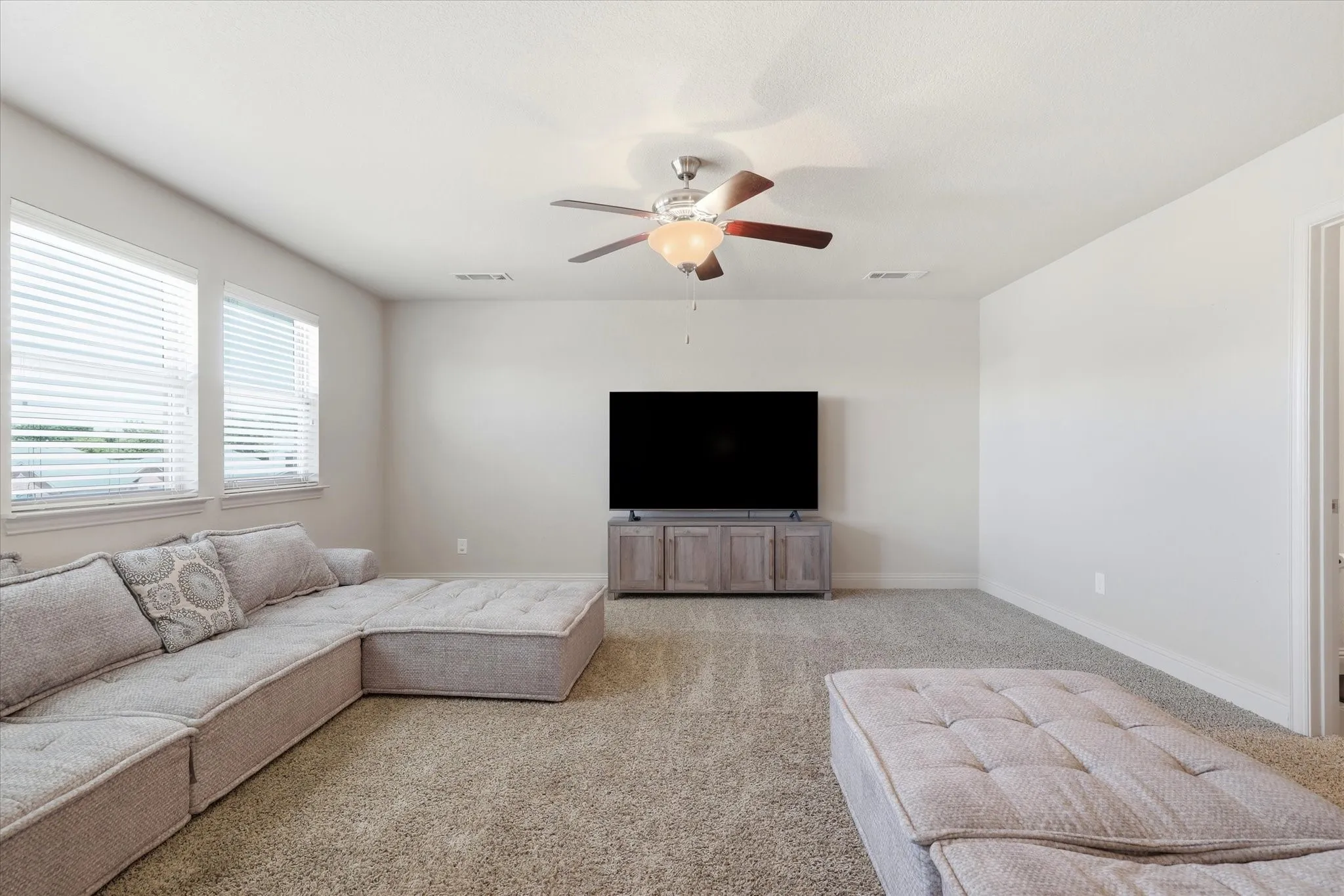 Carpeted room featuring multiple windows with blinds, a ceiling fan with integrated lighting, and a neutral wall color