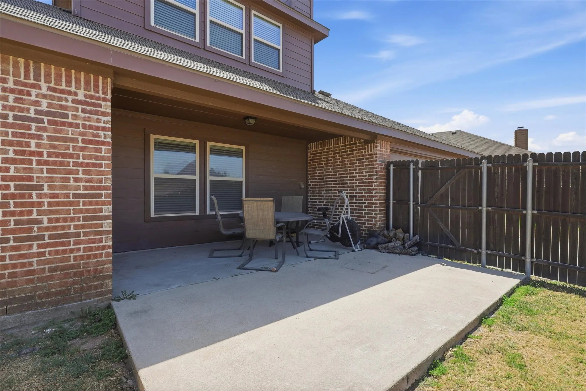 Covered concrete patio with brick and siding exterior and fenced perimeter