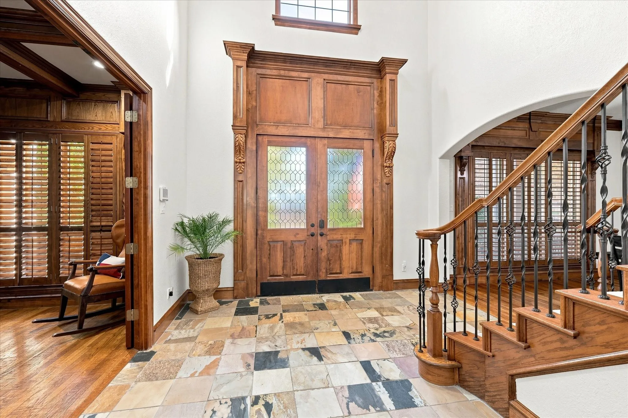Grand entry featuring a decorative solid wood front door with leaded glass, an ornate wood staircase with wrought iron balusters, and a slate tile floor