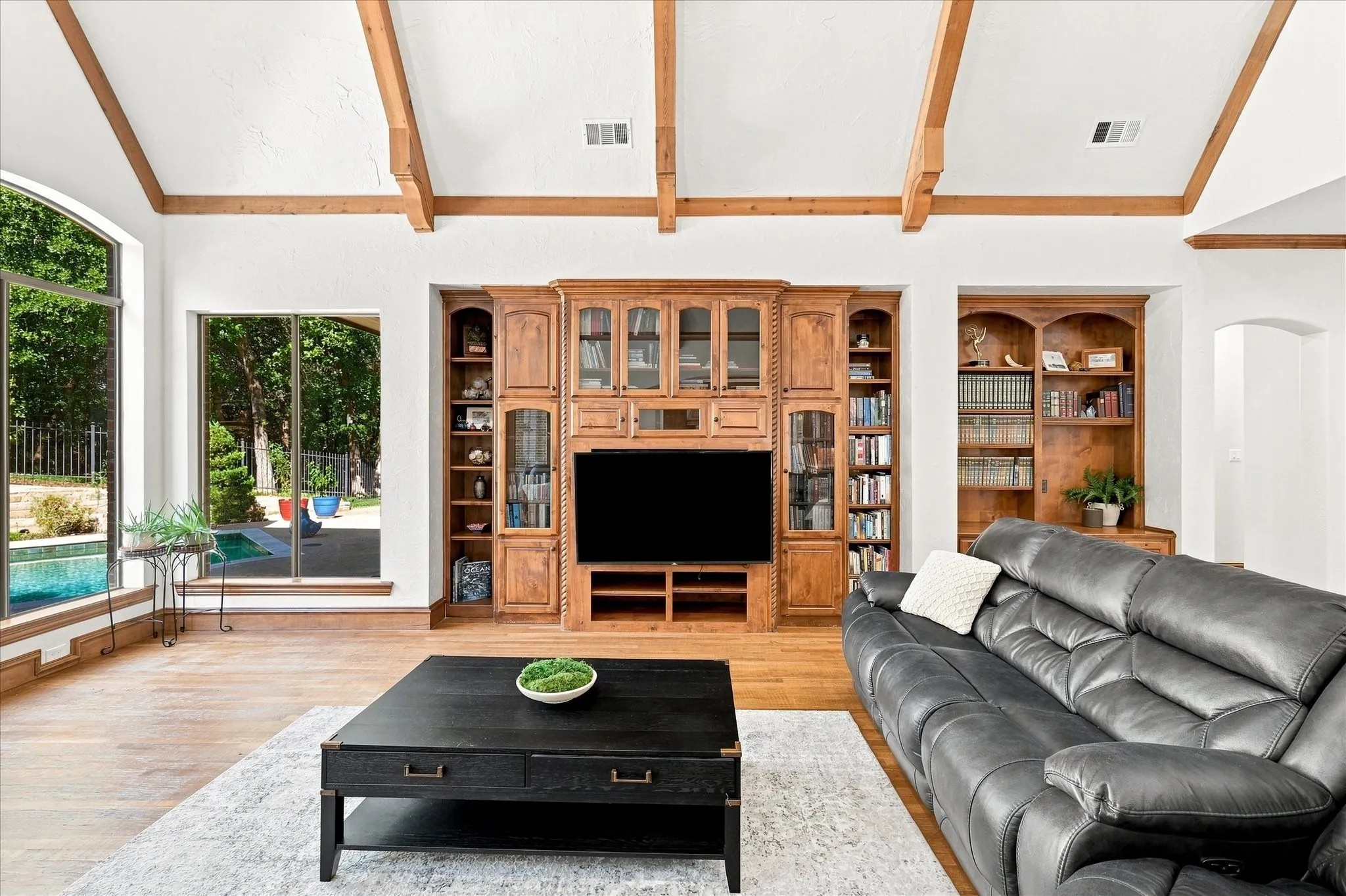 Vaulted ceiling with exposed wood beams, wood-finish flooring, built-in entertainment center, built-in shelving, and large windows