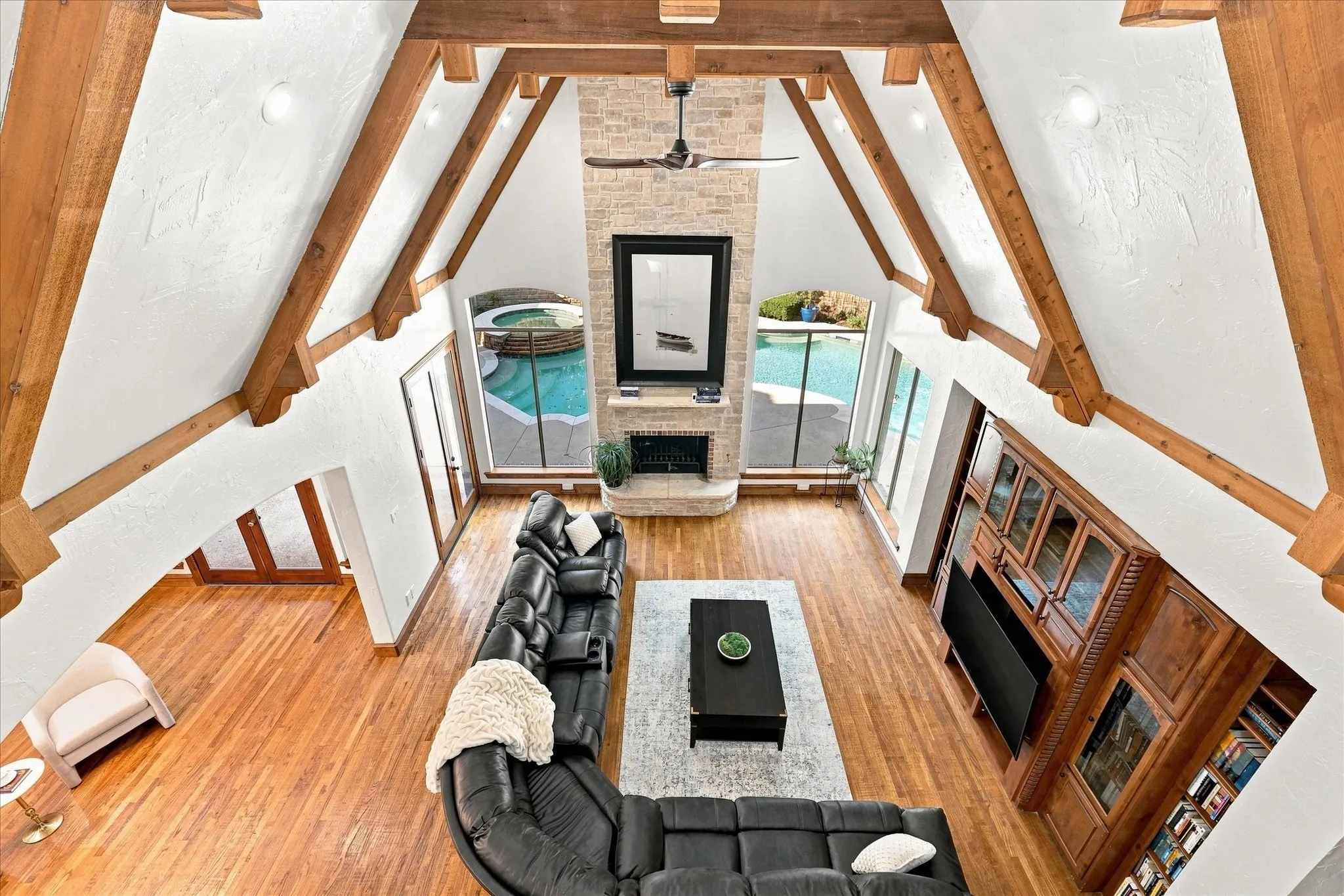 Vaulted wood-beamed ceilings, stone fireplace, wood-finish flooring, built-in entertainment center, and expansive windows