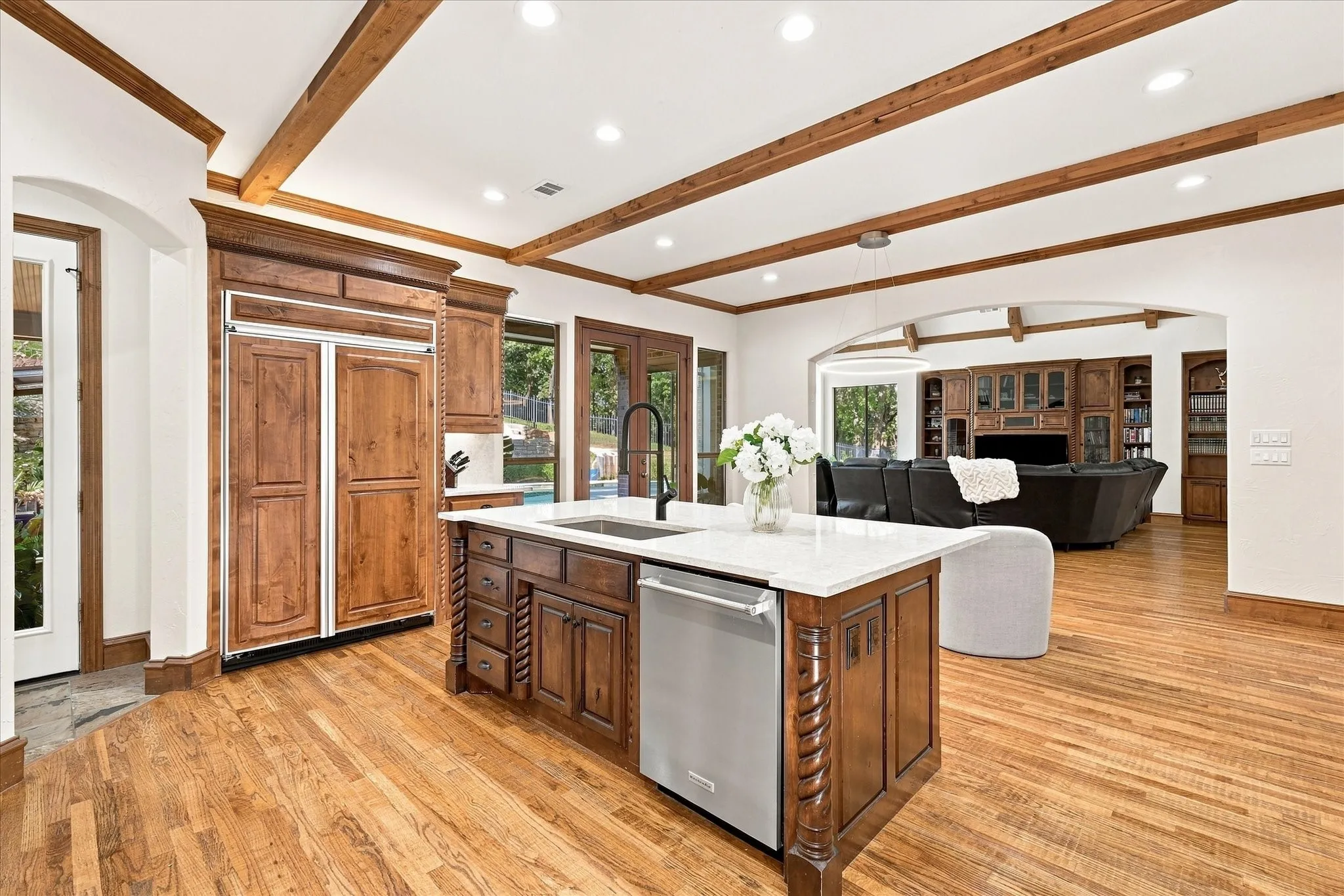 Hardwood flooring throughout, beamed ceiling, built-in refrigerator, kitchen island with sink and integrated dishwasher, arched entryway