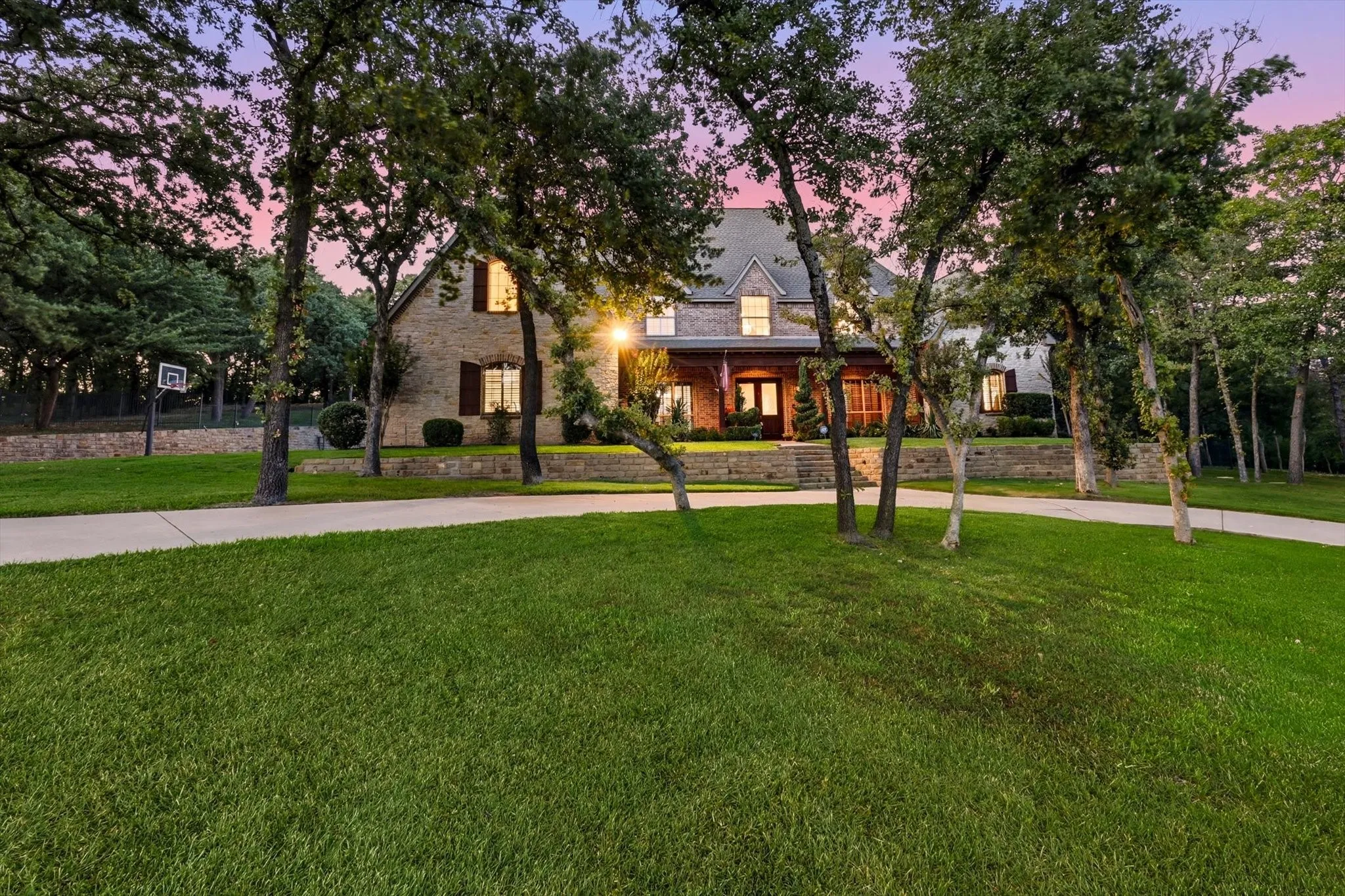 Stone exterior residence with a prominent covered front entry, multiple dormer windows, a concrete driveway, and mature landscaping